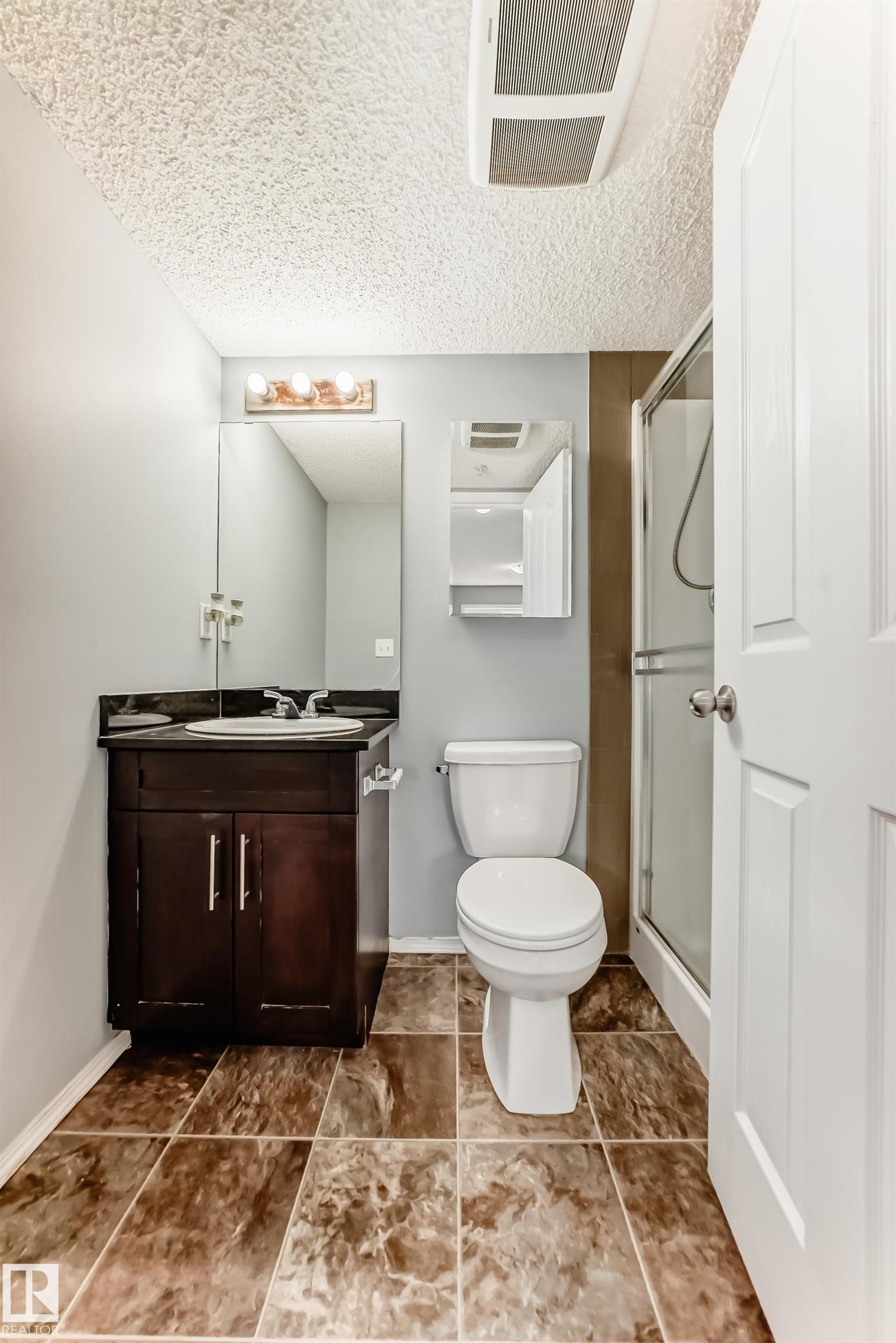 The bathroom features a vanity with a dark wood cabinet, a white toilet, and a stand-up shower with a glass enclosure - 101 530 Watt Boulevard, Edmonton, AB - Indoor Photo Showing Bathroom