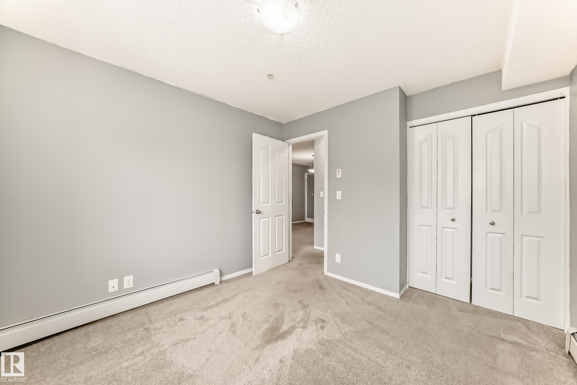 This room features carpeting, light gray walls, a white ceiling, and white bifold closet doors - 101 530 Watt Boulevard, Edmonton, AB - Indoor Photo Showing Other Room