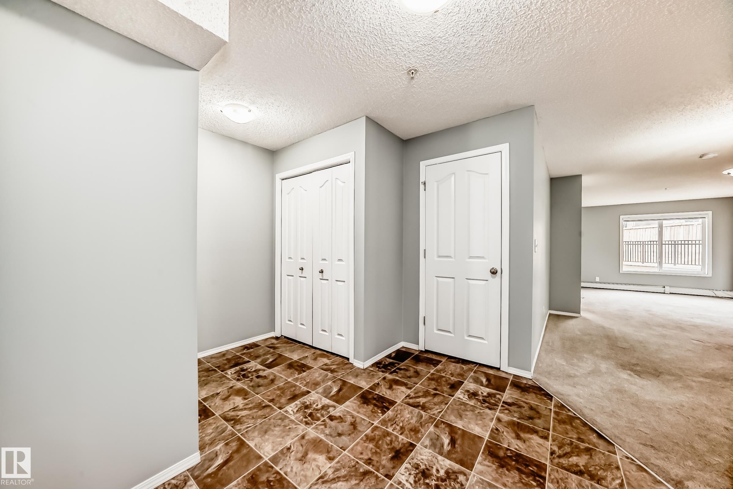 The property features a entryway with patterned floor tiles, white bi-fold closet doors, and a white interior door - 101 530 Watt Boulevard, Edmonton, AB - Indoor Photo Showing Other Room
