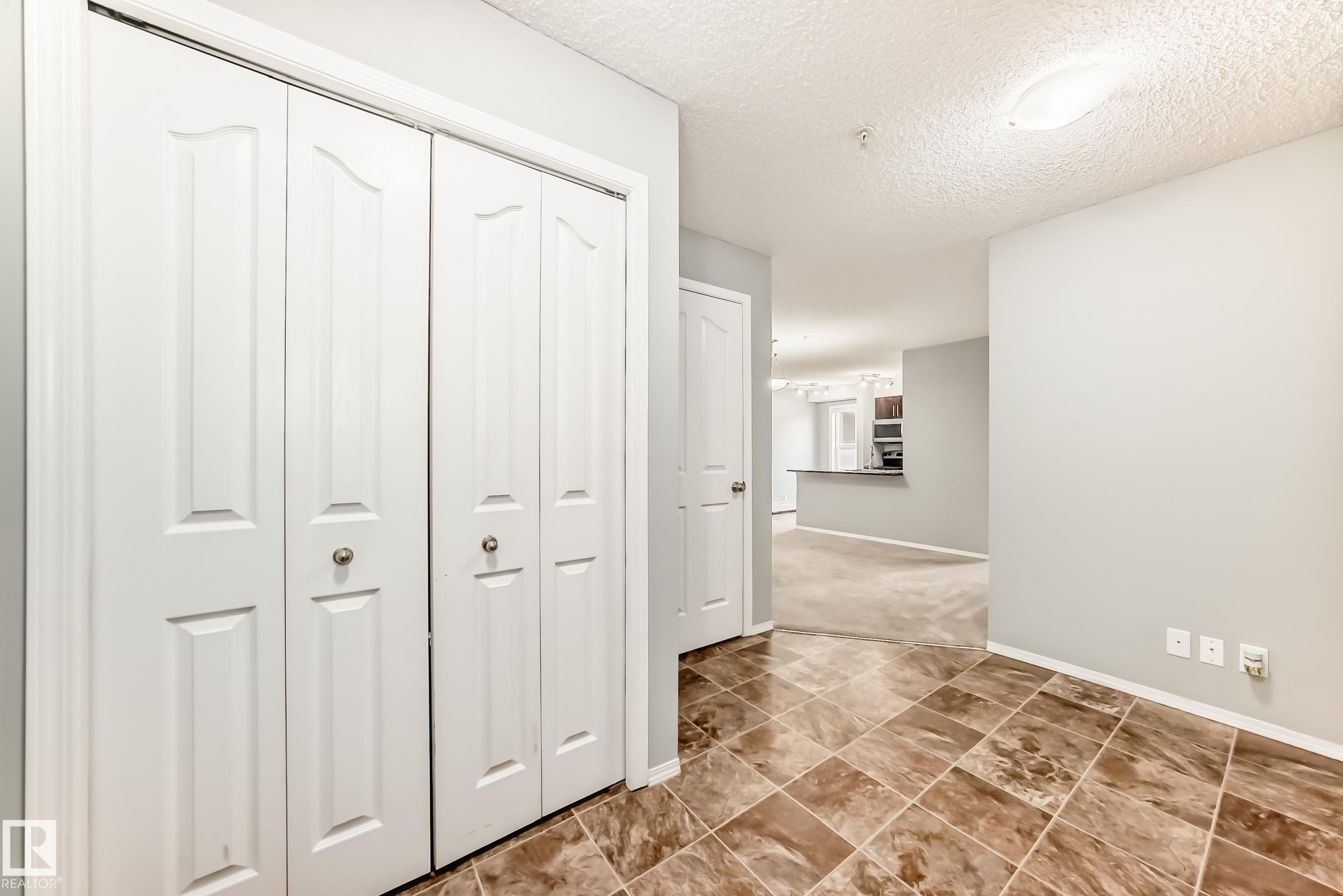 The entrance features durable tile flooring and bifold closet doors, with a clear sightline into the living area and kitchen - 101 530 Watt Boulevard, Edmonton, AB - Indoor Photo Showing Other Room