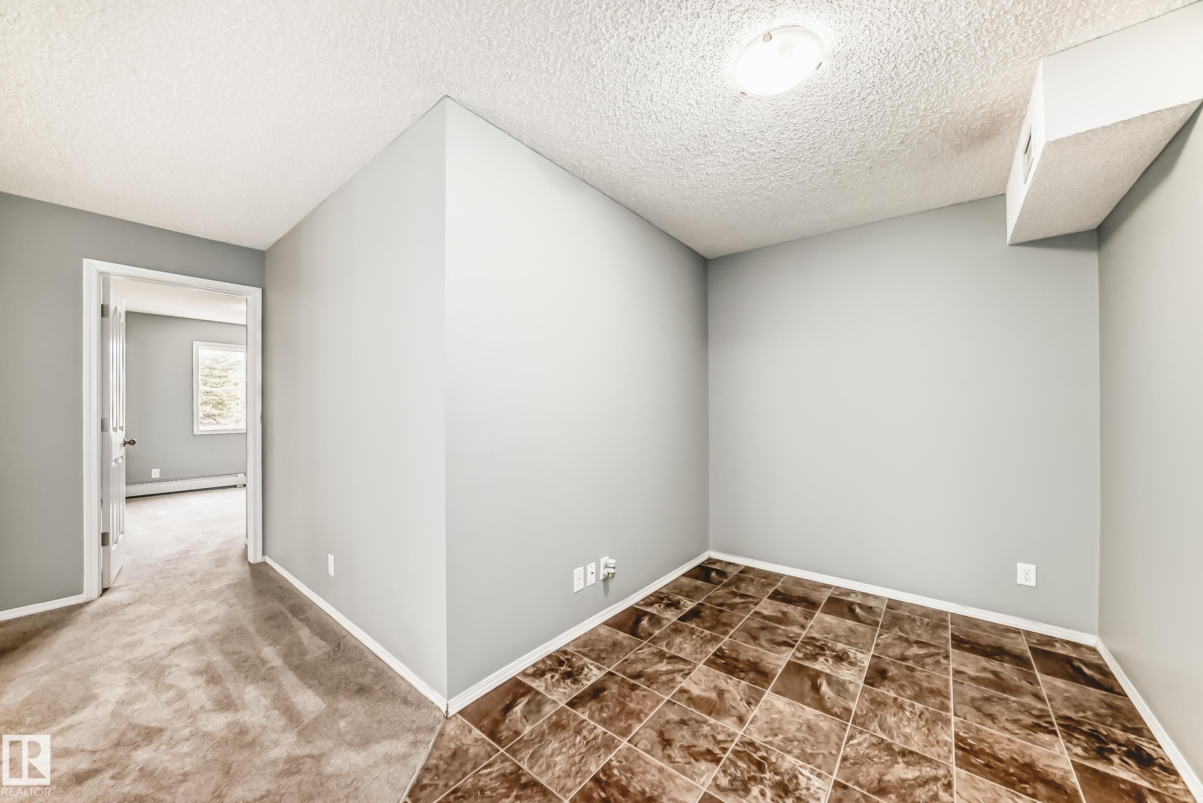 This space features neutral-toned walls, a textured ceiling, and a combination of carpeted and tiled flooring - 101 530 Watt Boulevard, Edmonton, AB - Indoor Photo Showing Other Room