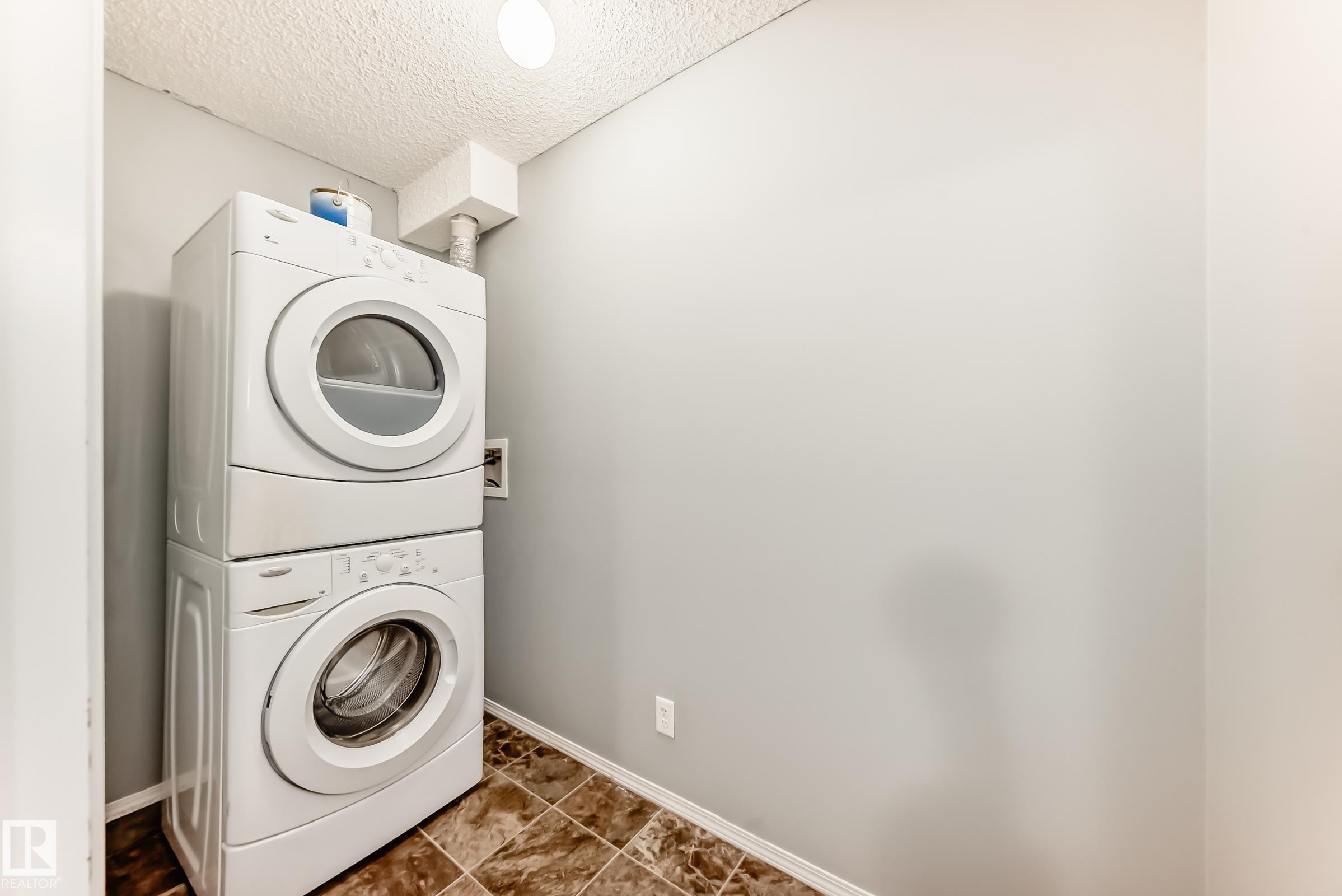 Dedicated laundry area featuring a white stackable washer and dryer, tiled flooring, and light gray walls - 101 530 Watt Boulevard, Edmonton, AB - Indoor Photo Showing Laundry Room