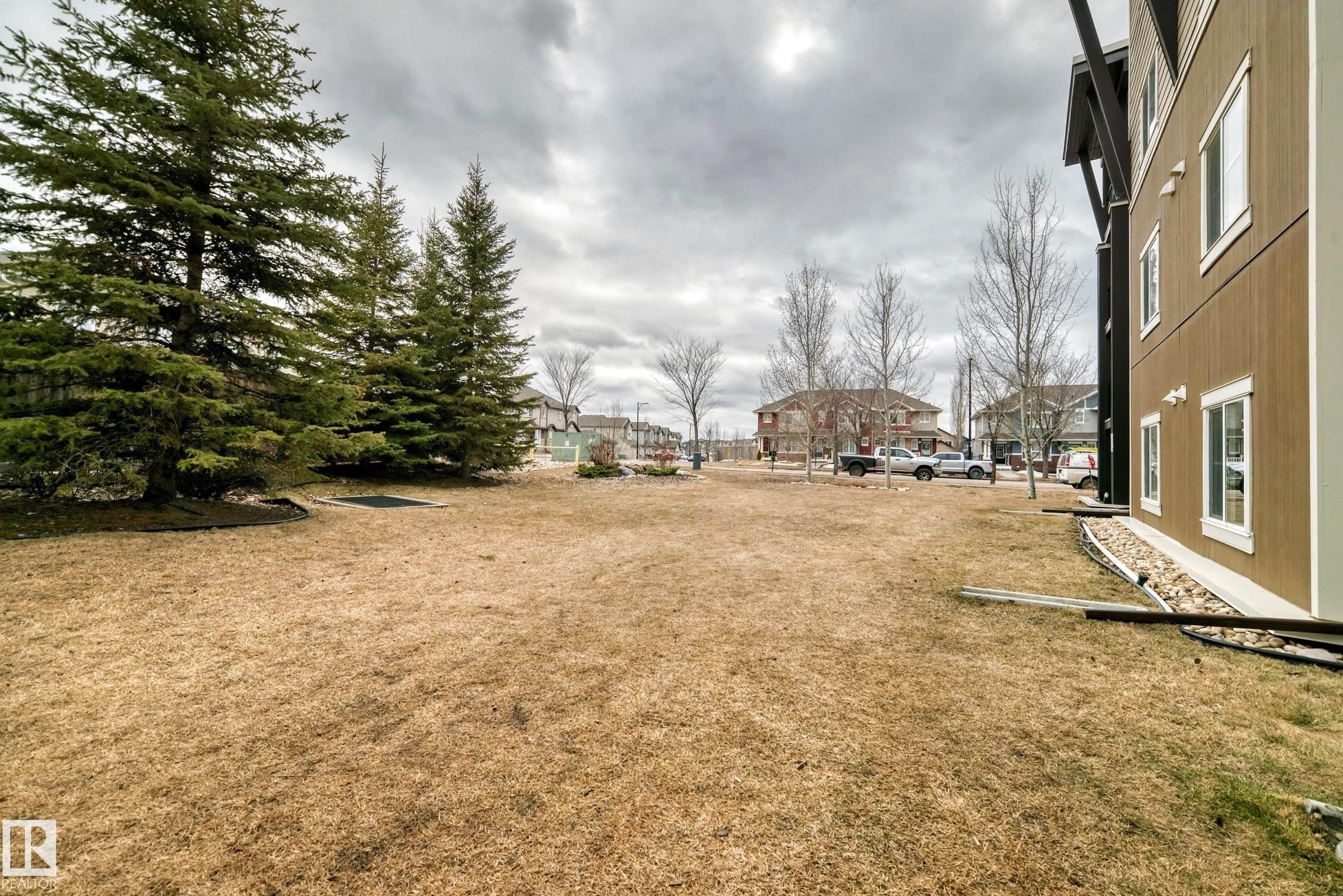 The property features a spacious yard with mature evergreen trees and a brown exterior siding - 101 530 Watt Boulevard, Edmonton, AB - Outdoor