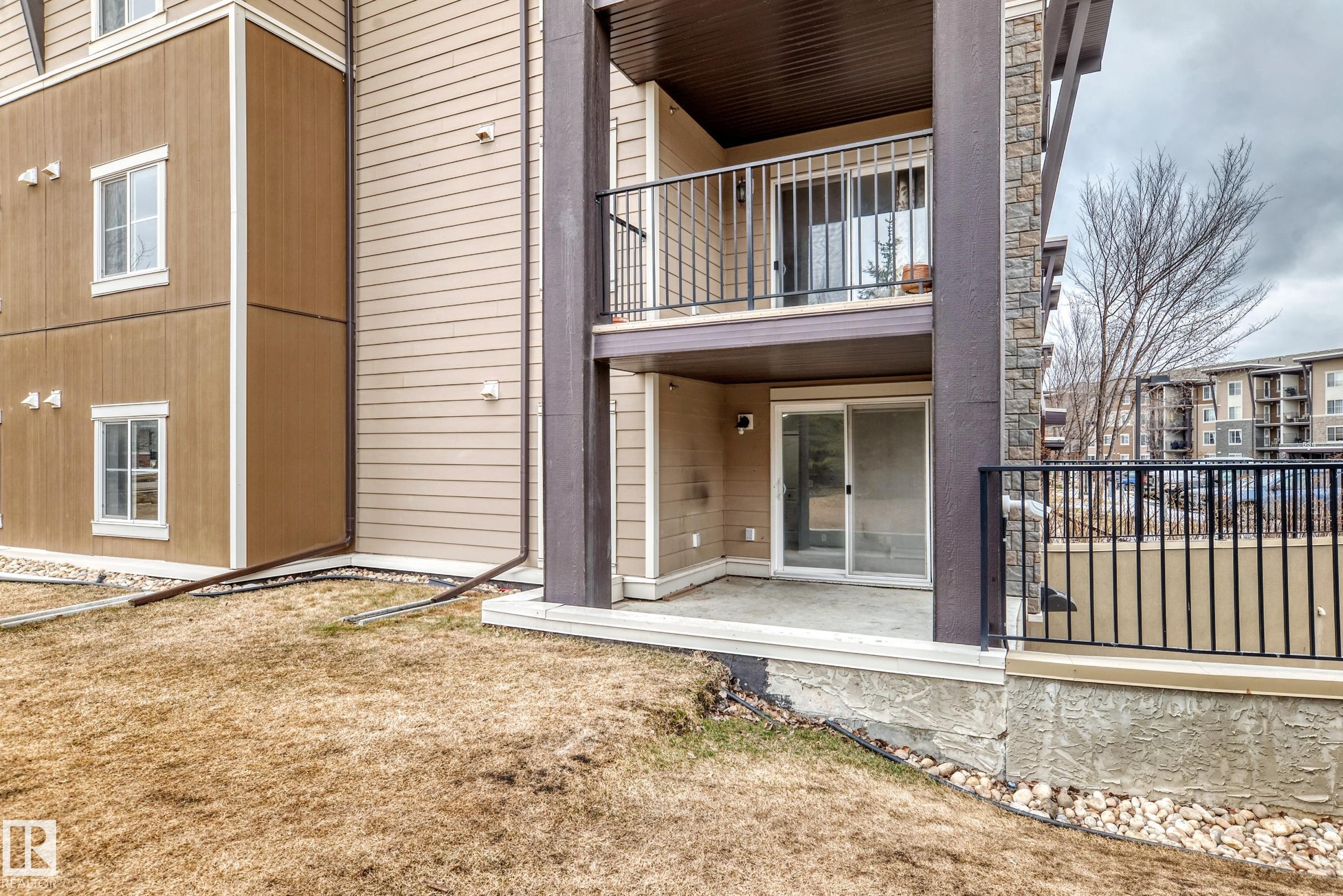 The property features a patio with a sliding glass door entry, and an upper balcony with black metal railings - 101 530 Watt Boulevard, Edmonton, AB - Outdoor With Exterior