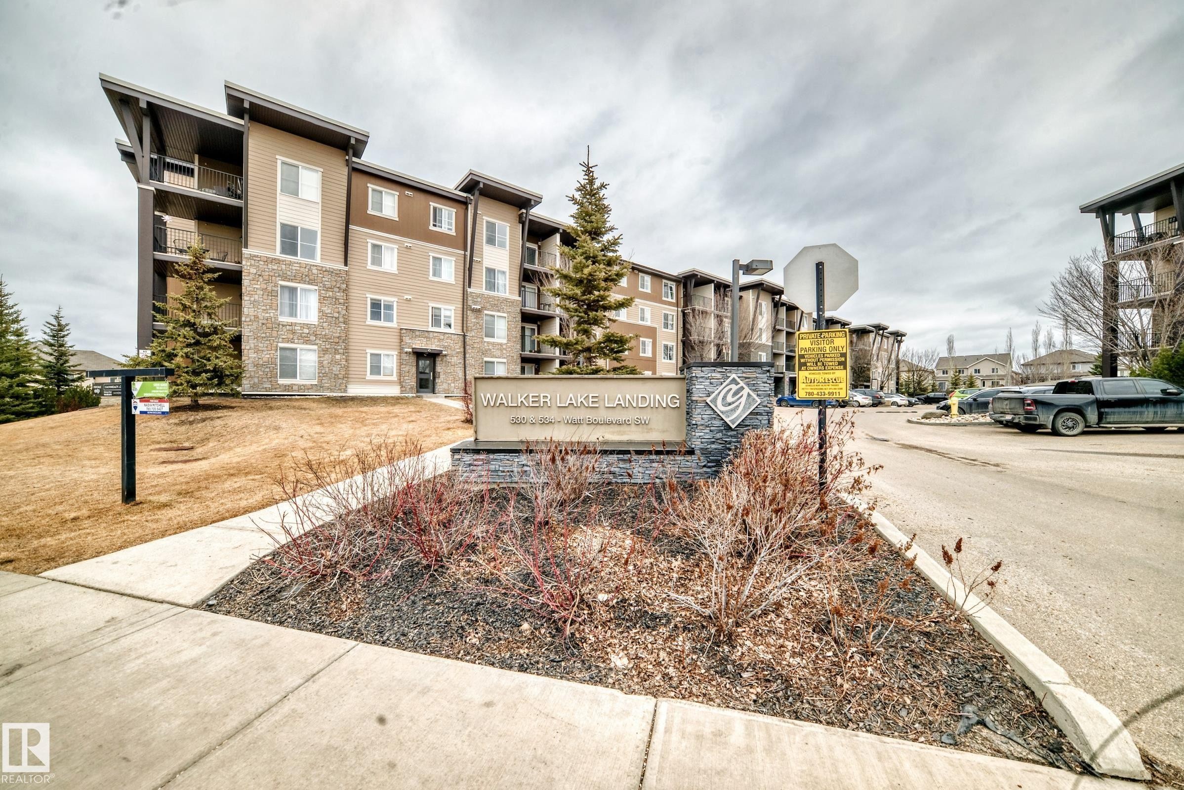 Exterior view of the property, featuring a multi-story building with balconies, a stone-clad sign for "WALKER LAKE LANDING," and a paved road - 101 530 Watt Boulevard, Edmonton, AB - Outdoor