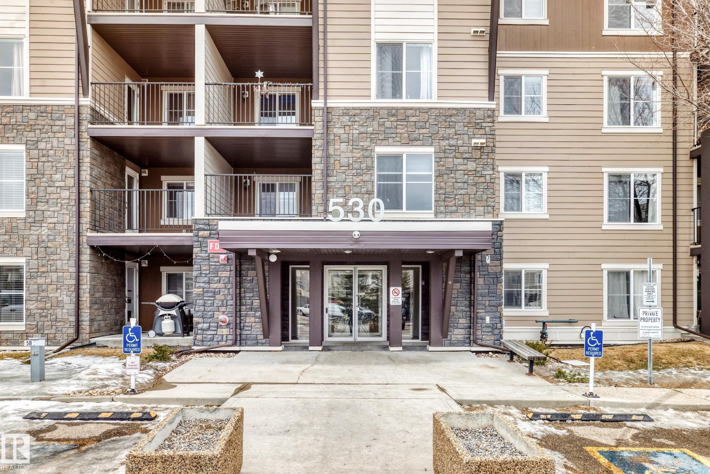 The property features a building with a stone and siding exterior, balconies with dark railings, and a welcoming main entrance with glass doors - 101 530 Watt Boulevard, Edmonton, AB - Outdoor With Facade