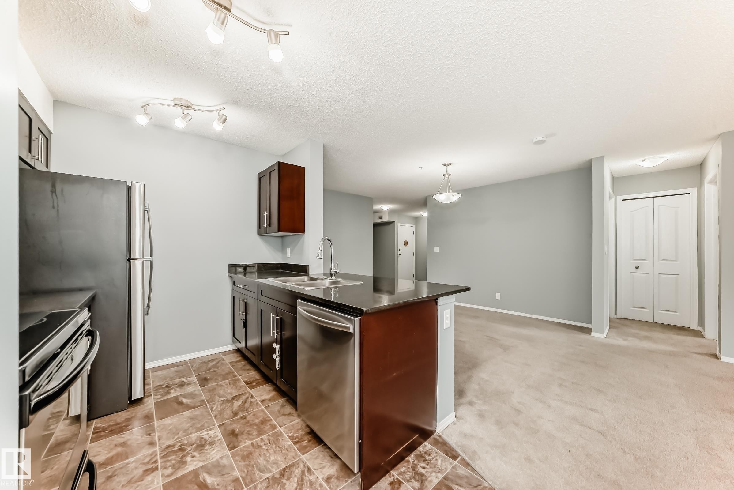 Kitchen featuring dark cabinetry, stainless steel appliances, and a tiled floor - 101 530 Watt Boulevard, Edmonton, AB - Indoor Photo Showing Kitchen With Double Sink