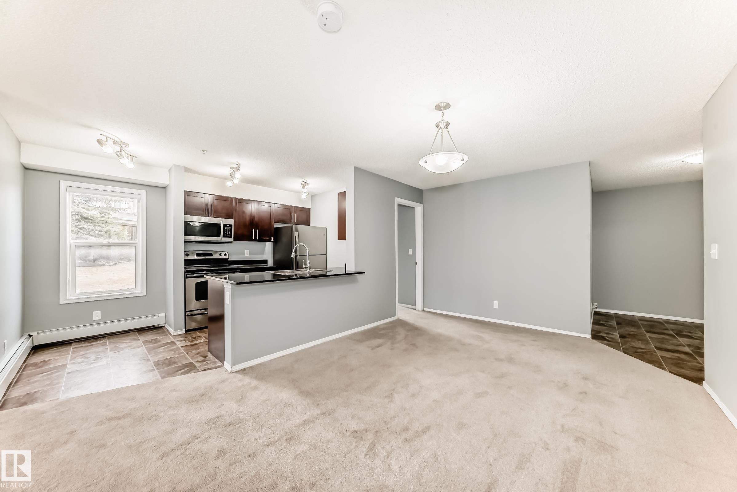 The open concept living area features a kitchen with dark cabinetry, stainless steel appliances, and a breakfast bar - 101 530 Watt Boulevard, Edmonton, AB - Indoor Photo Showing Kitchen