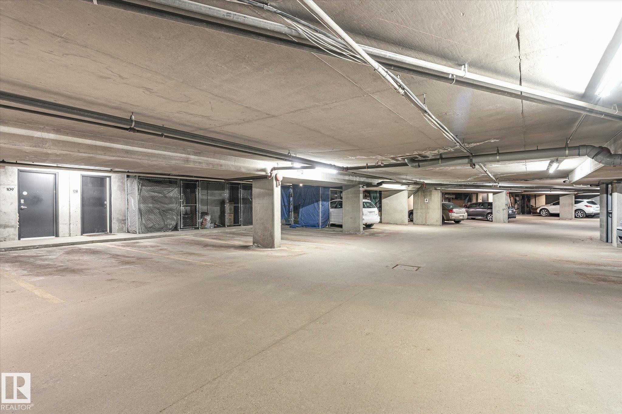 Underground concrete parking garage featuring ample parking spaces, exposed utility conduits, and integrated ceiling lighting - 108 10105 95 Street, Edmonton, AB - Indoor Photo Showing Garage