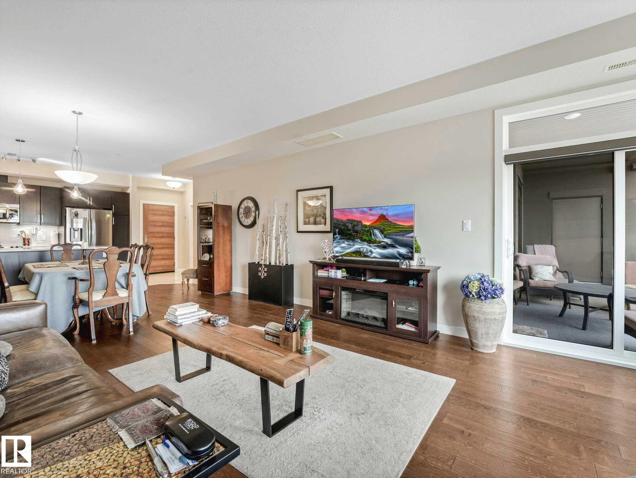 Open-concept living space featuring wood-finish flooring, recessed lighting, and a sliding glass door leading to an outdoor area - 213 625 Leger Way, Edmonton, AB - Indoor Photo Showing Living Room