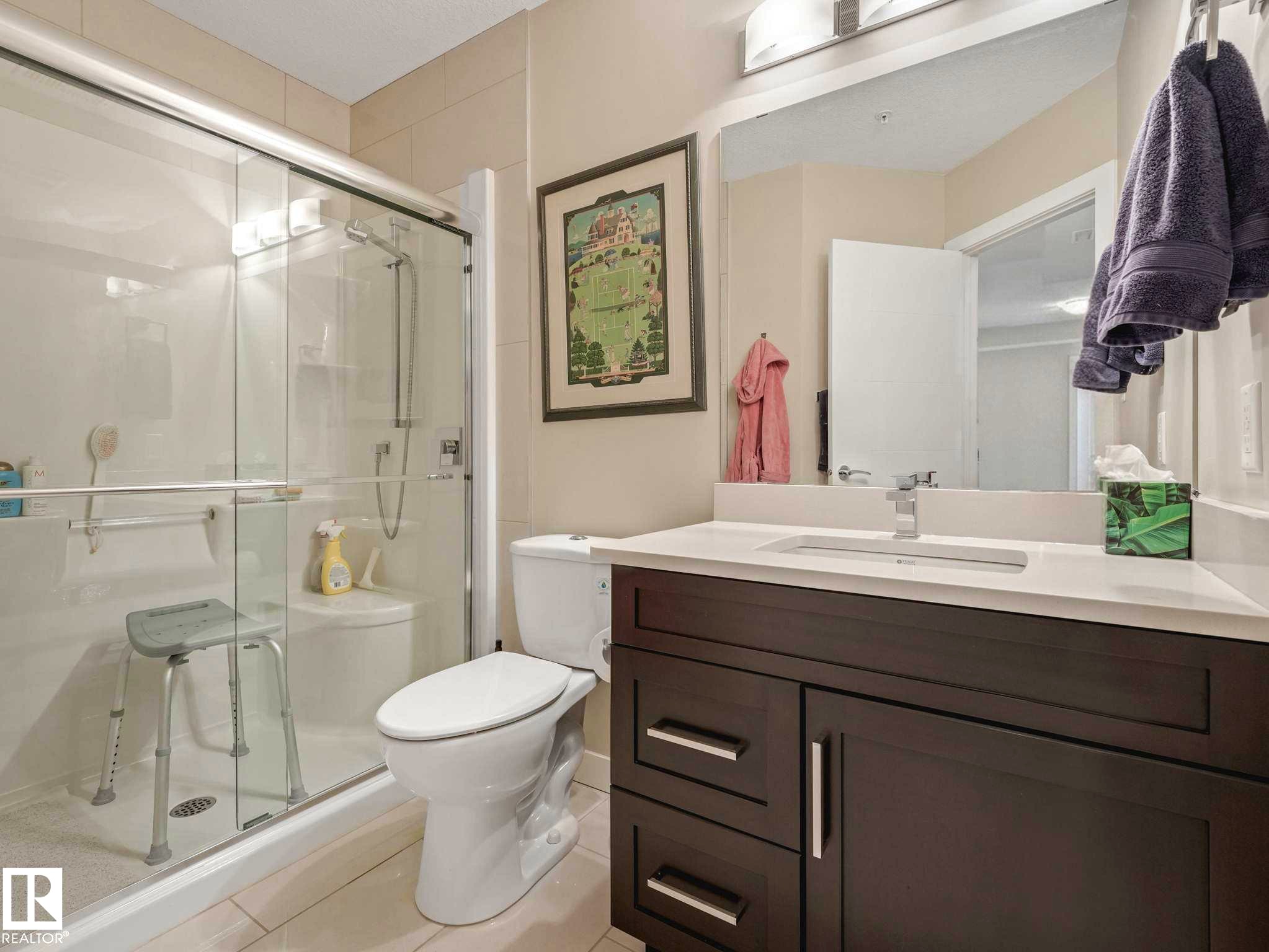Contemporary bathroom featuring a dark wood-finish vanity with a white countertop and undermount sink - 213 625 Leger Way, Edmonton, AB - Indoor Photo Showing Bathroom