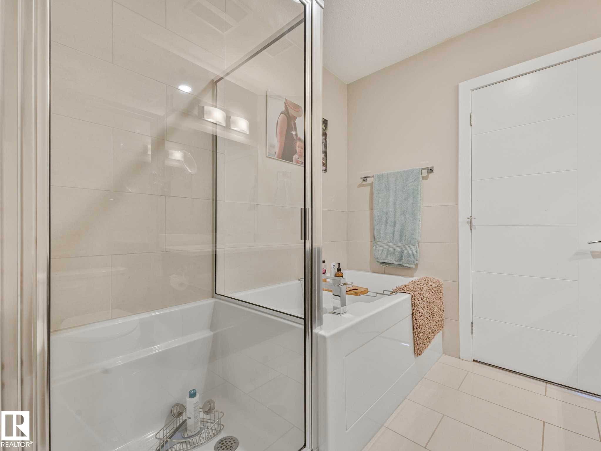 Bathtub with integrated shower, glass shower enclosure, and tiled walls - 213 625 Leger Way, Edmonton, AB - Indoor Photo Showing Bathroom