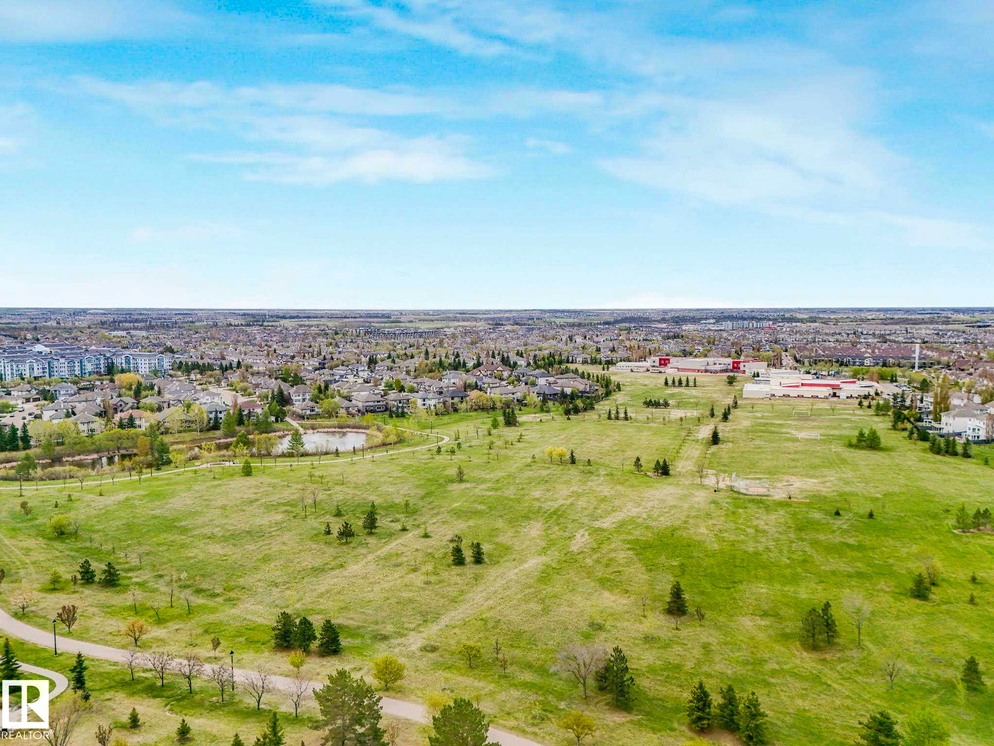Expansive green space with walking paths, bordered by residential areas and commercial structures - 213 625 Leger Way, Edmonton, AB - Outdoor With View