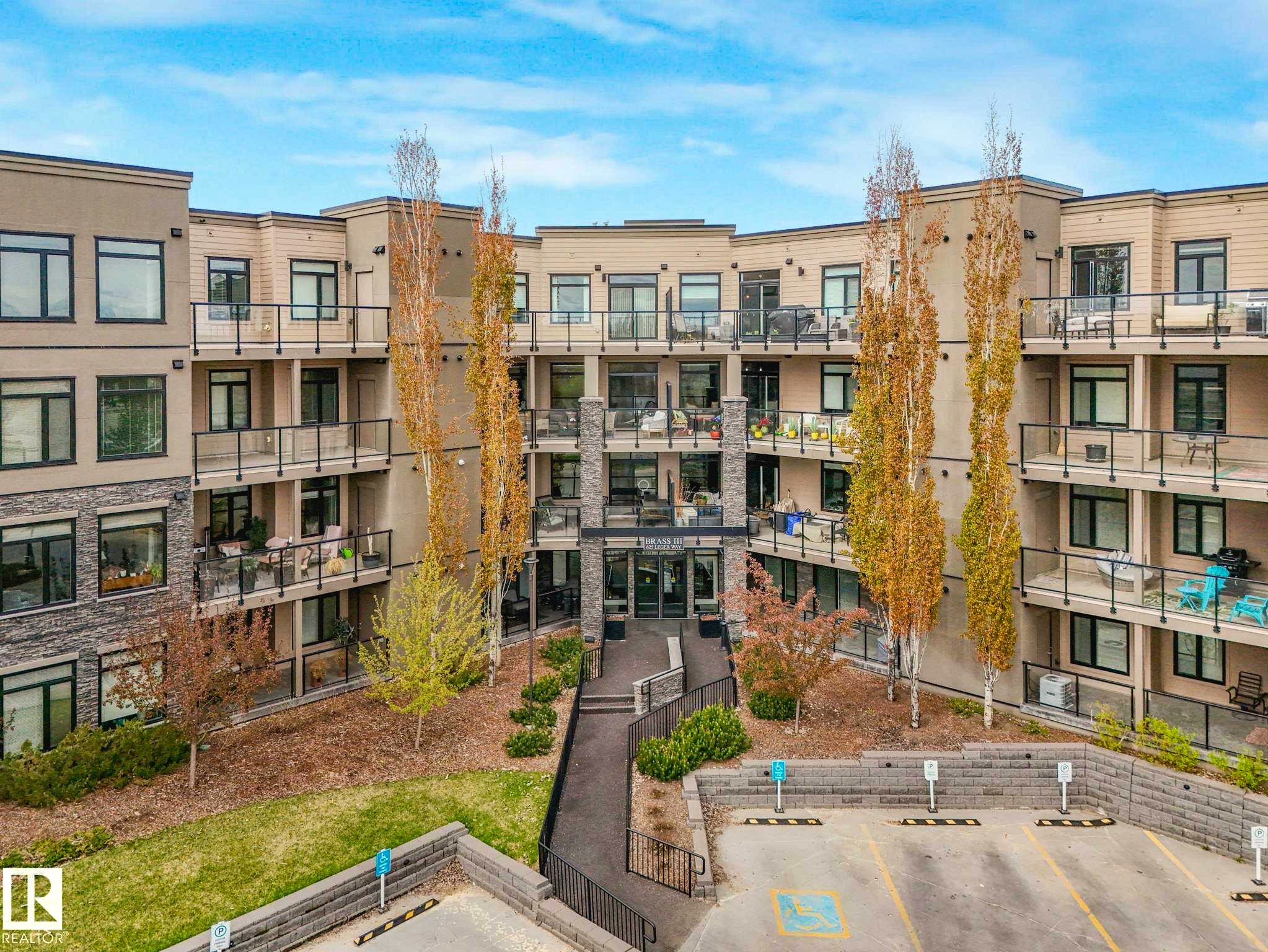 Multi-story building featuring a stone and siding exterior, private balconies with glass railings, and expansive windows - 213 625 Leger Way, Edmonton, AB - Outdoor With Balcony