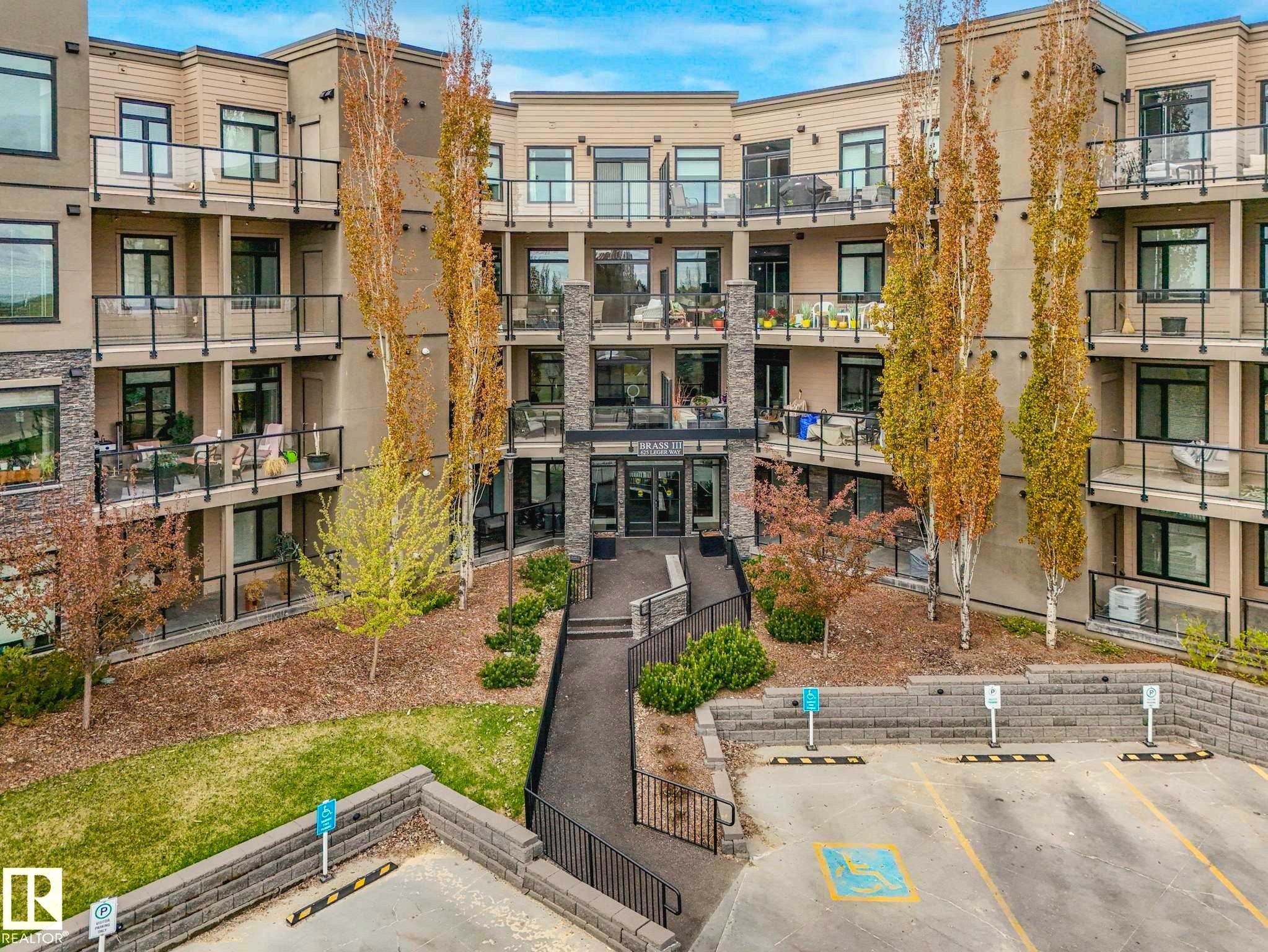 Multi-story residential building featuring stone accents and light-toned siding - 213 625 Leger Way, Edmonton, AB - Outdoor With Balcony