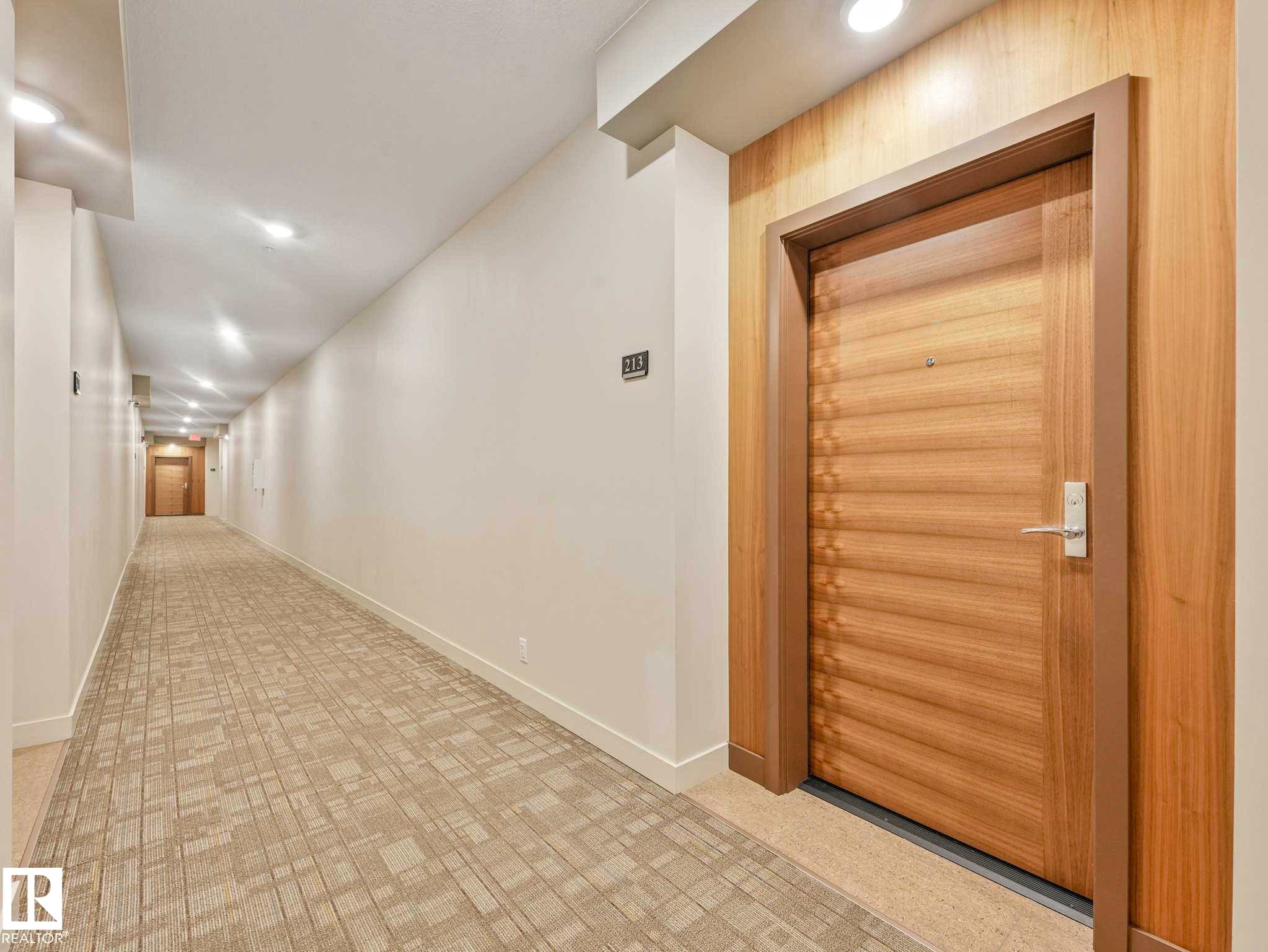 Entry door featuring a natural wood finish with horizontal detailing, framed by a light wood trim - 213 625 Leger Way, Edmonton, AB - Indoor Photo Showing Other Room