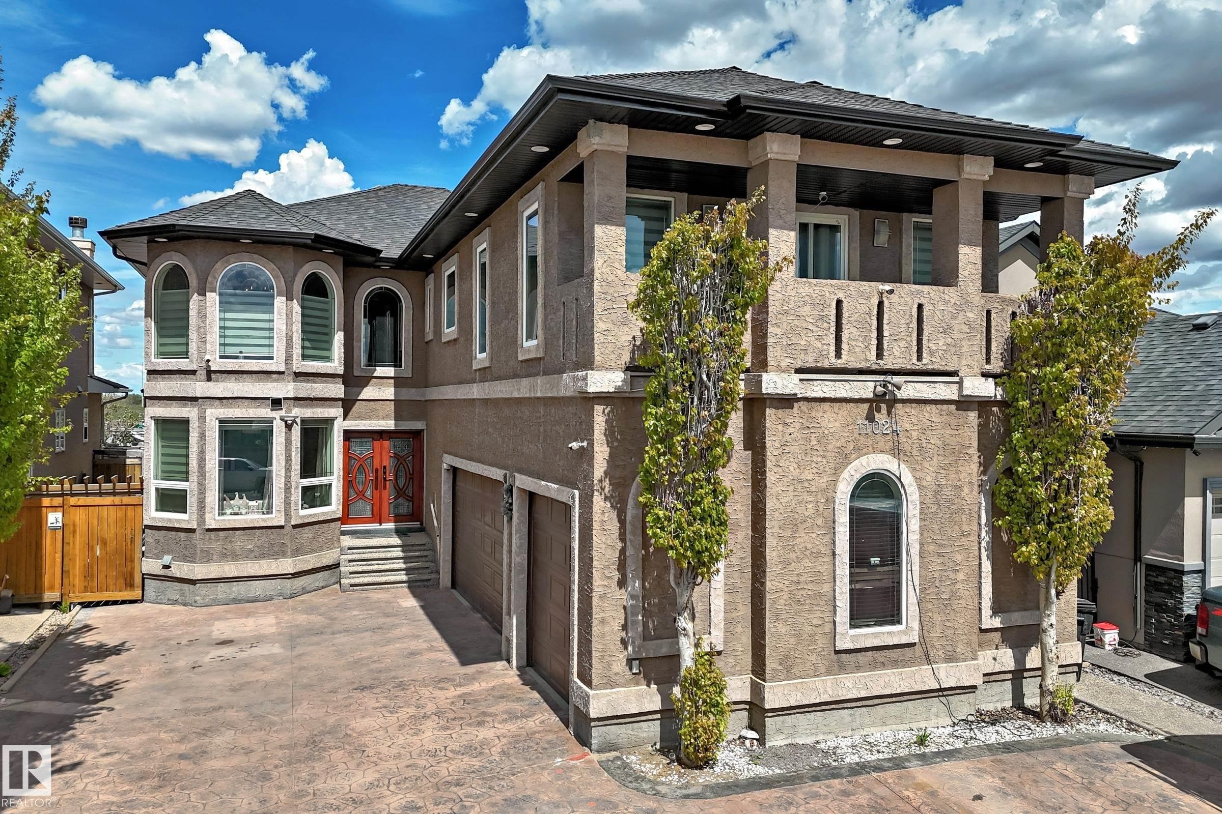 Stucco exterior with an upper-level balcony, arched and rectangular windows, and a stamped concrete driveway - 11024 179 Avenue, Edmonton, AB - Outdoor With Facade