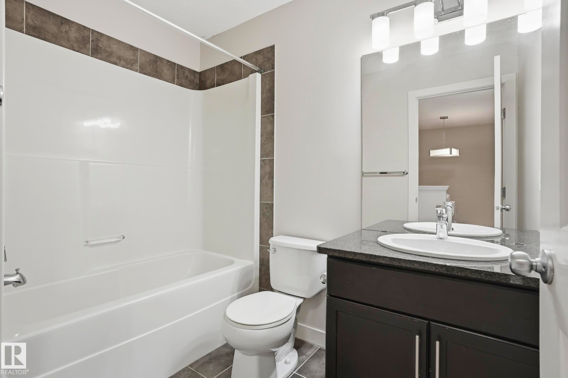 Contemporary bathroom featuring a white tub/shower combination with dark accent tiling, a dark wood-finish vanity with a light speckled countertop, an undermount sink, and a large wall-mounted mirror - 2917 16A Avenue, Edmonton, AB - Indoor Photo Showing Bathroom