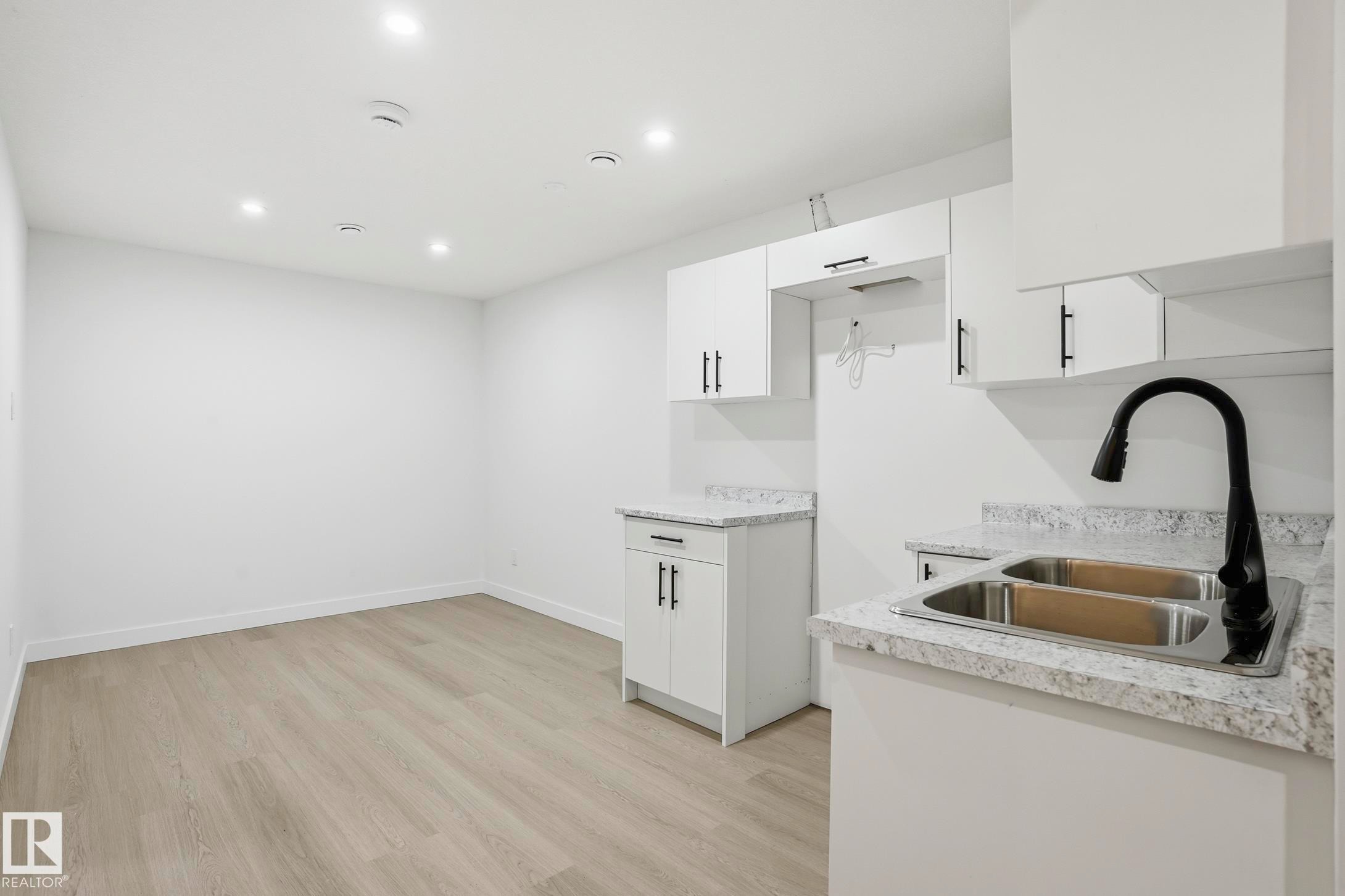 Kitchenette featuring white cabinetry with matte black hardware, dual stainless steel sink, black gooseneck faucet, and light-toned countertops - 2917 16A Avenue, Edmonton, AB - Indoor Photo Showing Kitchen With Double Sink