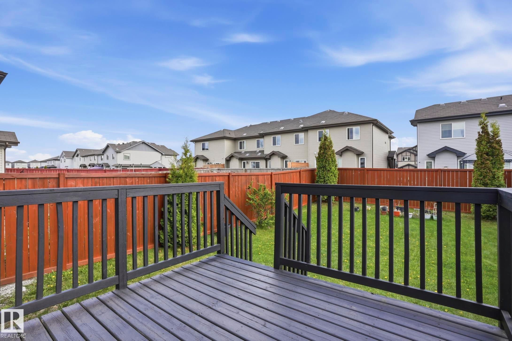 Spacious backyard featuring a dark-stained wood deck with black railings, a full-height wood fence, and a manicured lawn - 2917 16A Avenue, Edmonton, AB - Outdoor With Deck Patio Veranda With Exterior