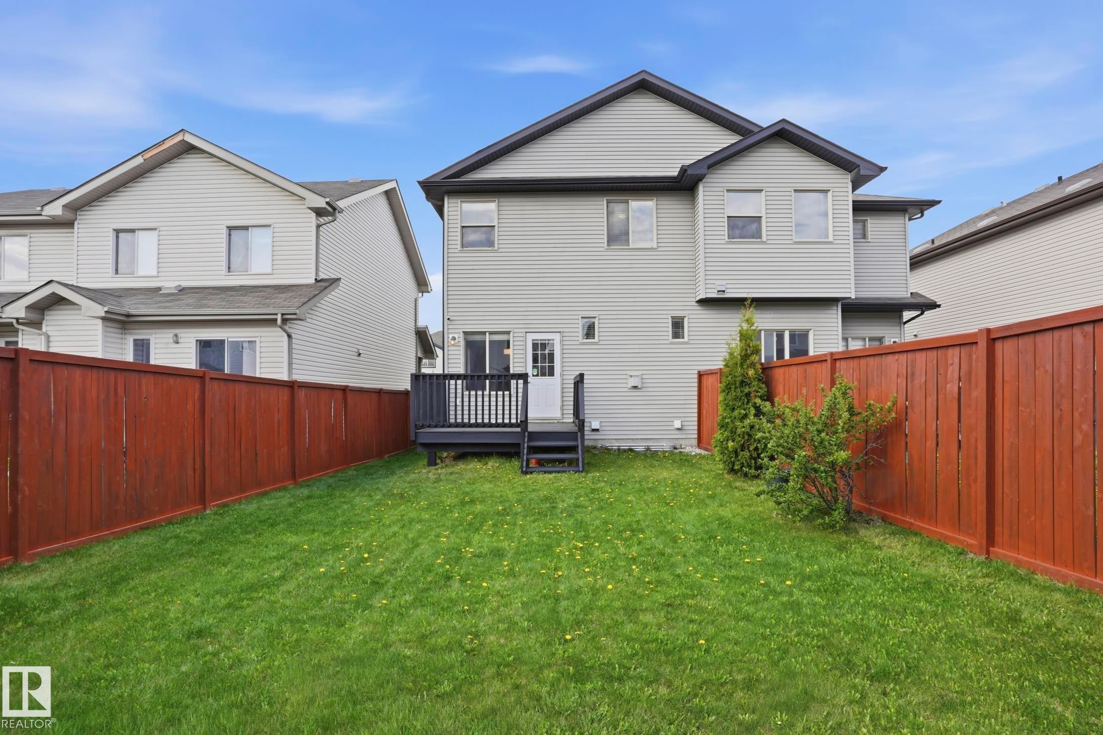 Expansive rear lawn featuring a dark wood deck, white egress door, and full perimeter wood fencing - 2917 16A Avenue, Edmonton, AB - Outdoor