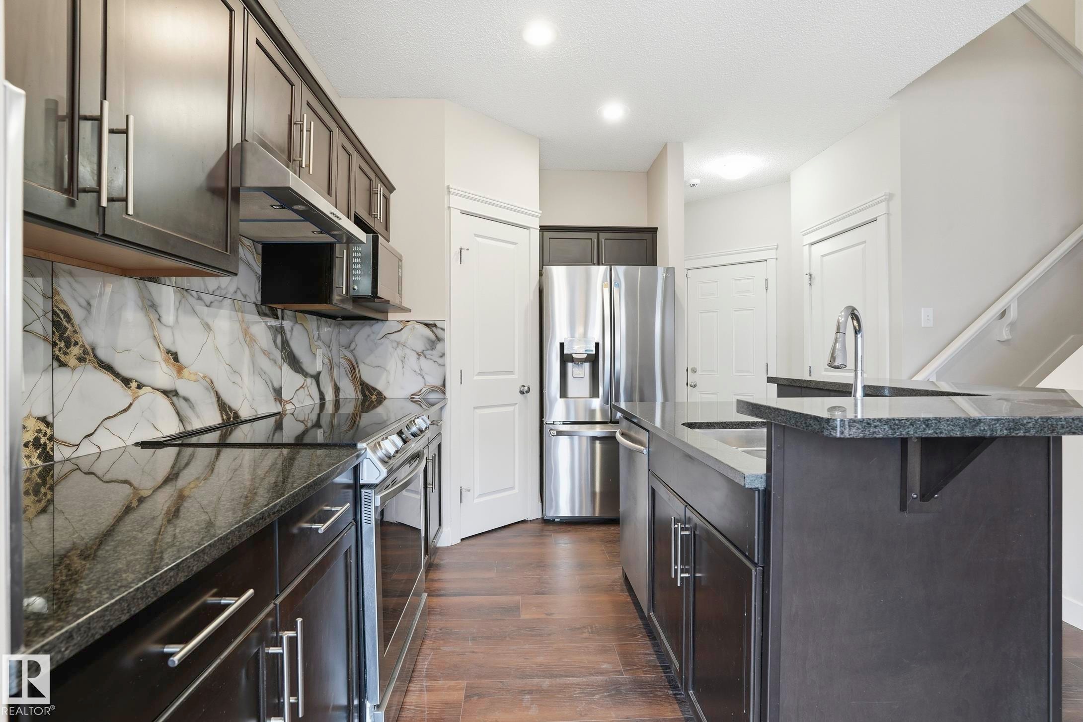 Kitchen featuring dark cabinetry, stainless steel appliances, and a contrasting marble-patterned backsplash - 2917 16A Avenue, Edmonton, AB - Indoor Photo Showing Kitchen With Stainless Steel Kitchen With Upgraded Kitchen