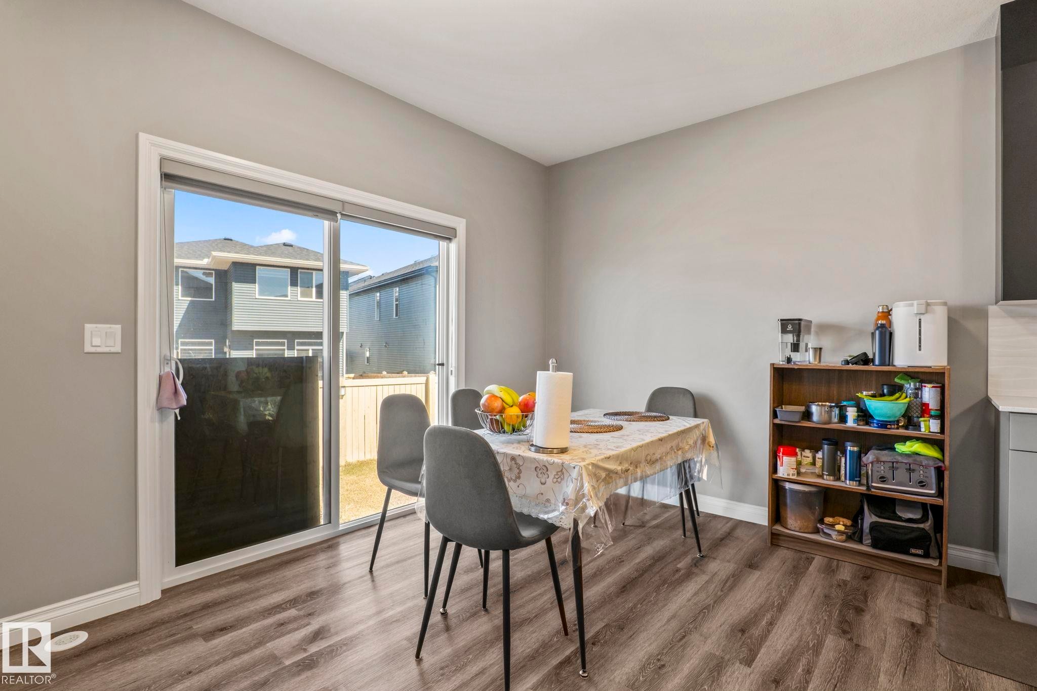 Dining area featuring wood-finish flooring, light gray walls, white baseboards, and a glass sliding door - 5142 23A Avenue, Edmonton, AB - Indoor Photo Showing Dining Room