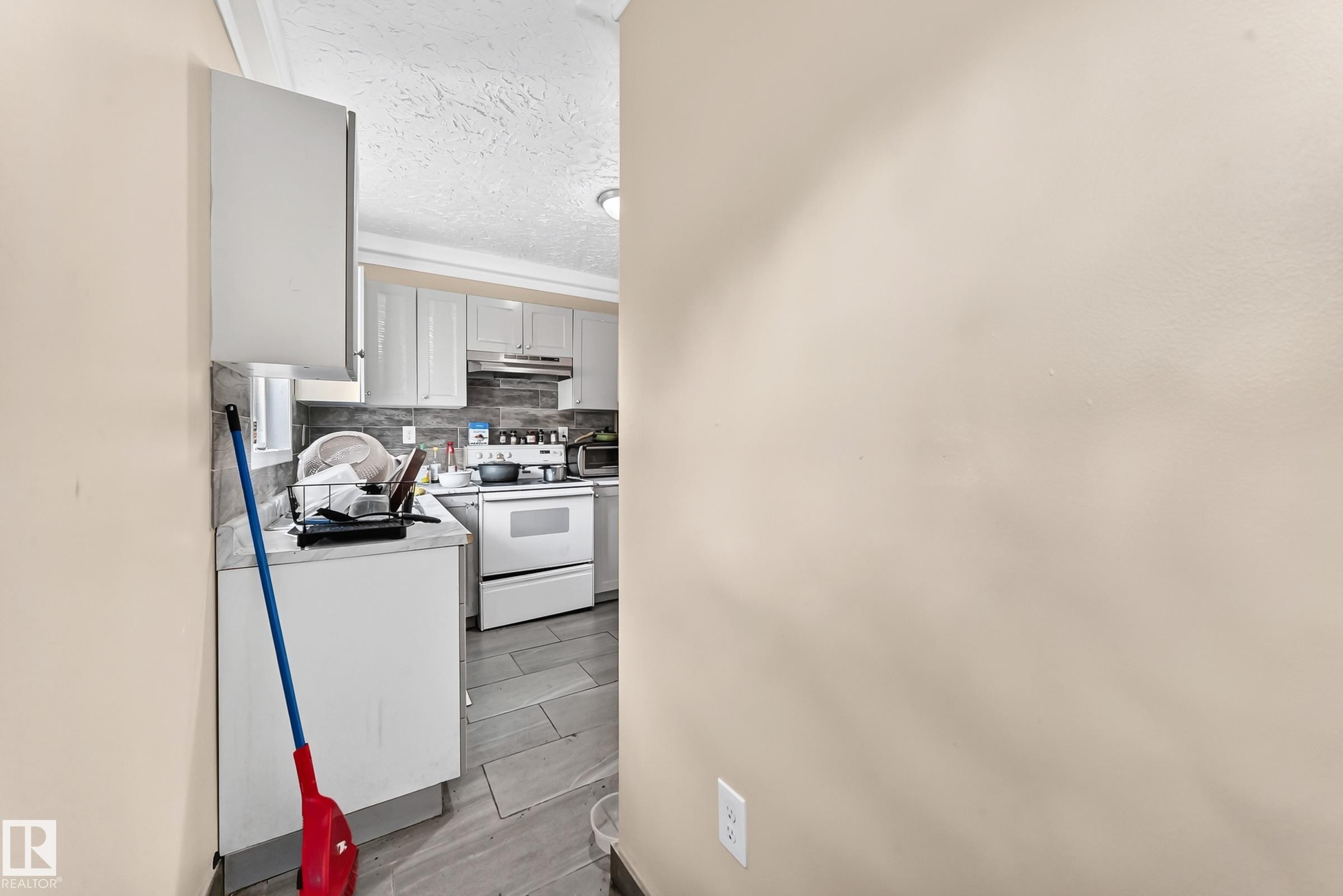 Kitchen featuring light-toned cabinetry, a stainless steel range hood, and tile flooring - 12627 71 Street Nw, Edmonton, AB