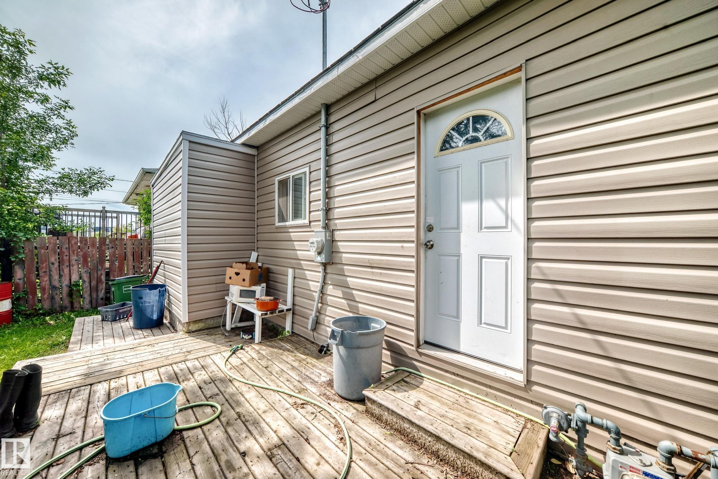 Exterior featuring horizontal siding, a white entry door with an arched window insert, and a wooden deck - 12627 71 Street Nw, Edmonton, AB