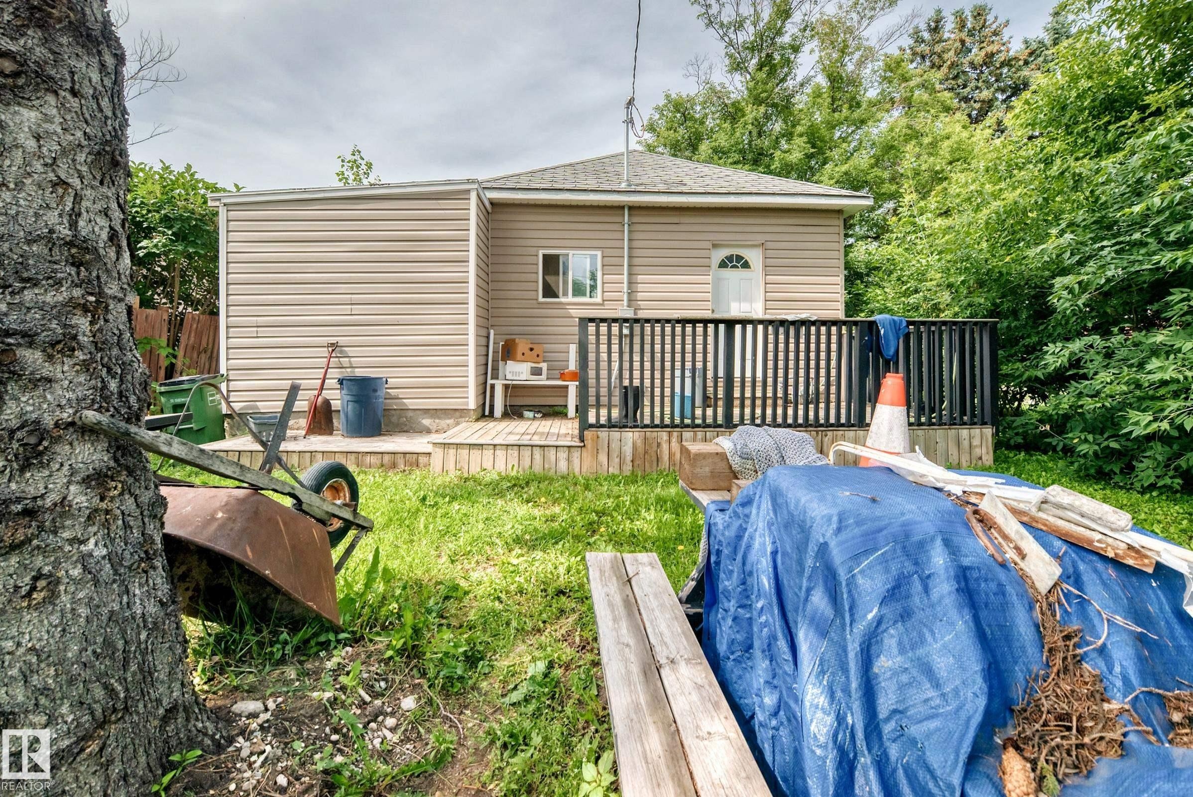 Exterior featuring tan siding, a wooden deck with black railings, and a white paneled door - 12627 71 Street Nw, Edmonton, AB