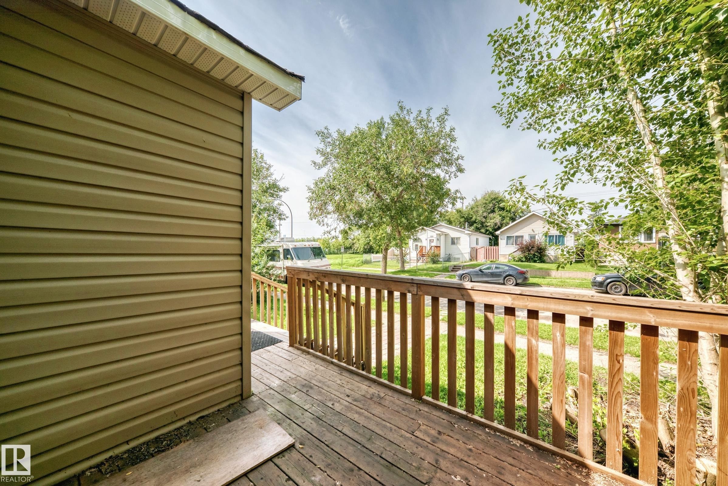 Exterior featuring horizontal siding, wooden deck, wooden railing, and mature trees - 12627 71 Street Nw, Edmonton, AB