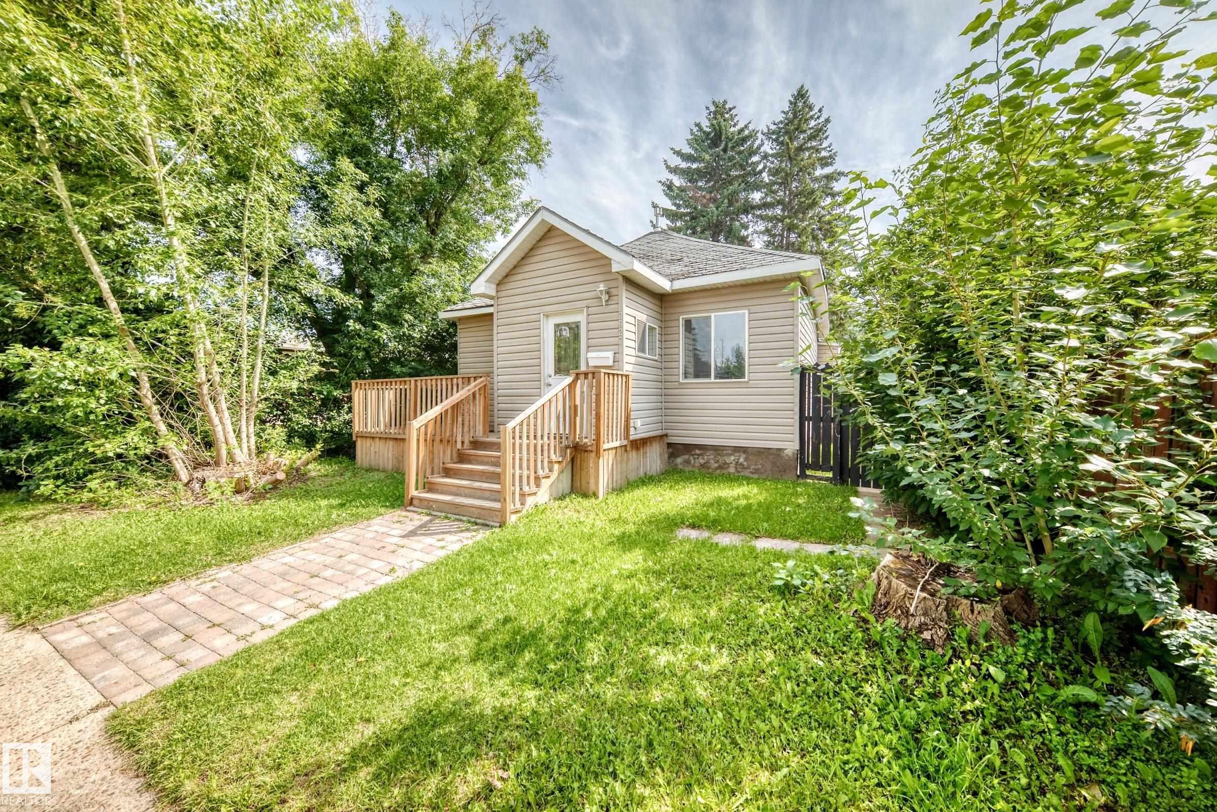 Exterior featuring horizontal siding, a wood-finish deck with stairs, a front entry door, and a paver pathway - 12627 71 Street Nw, Edmonton, AB
