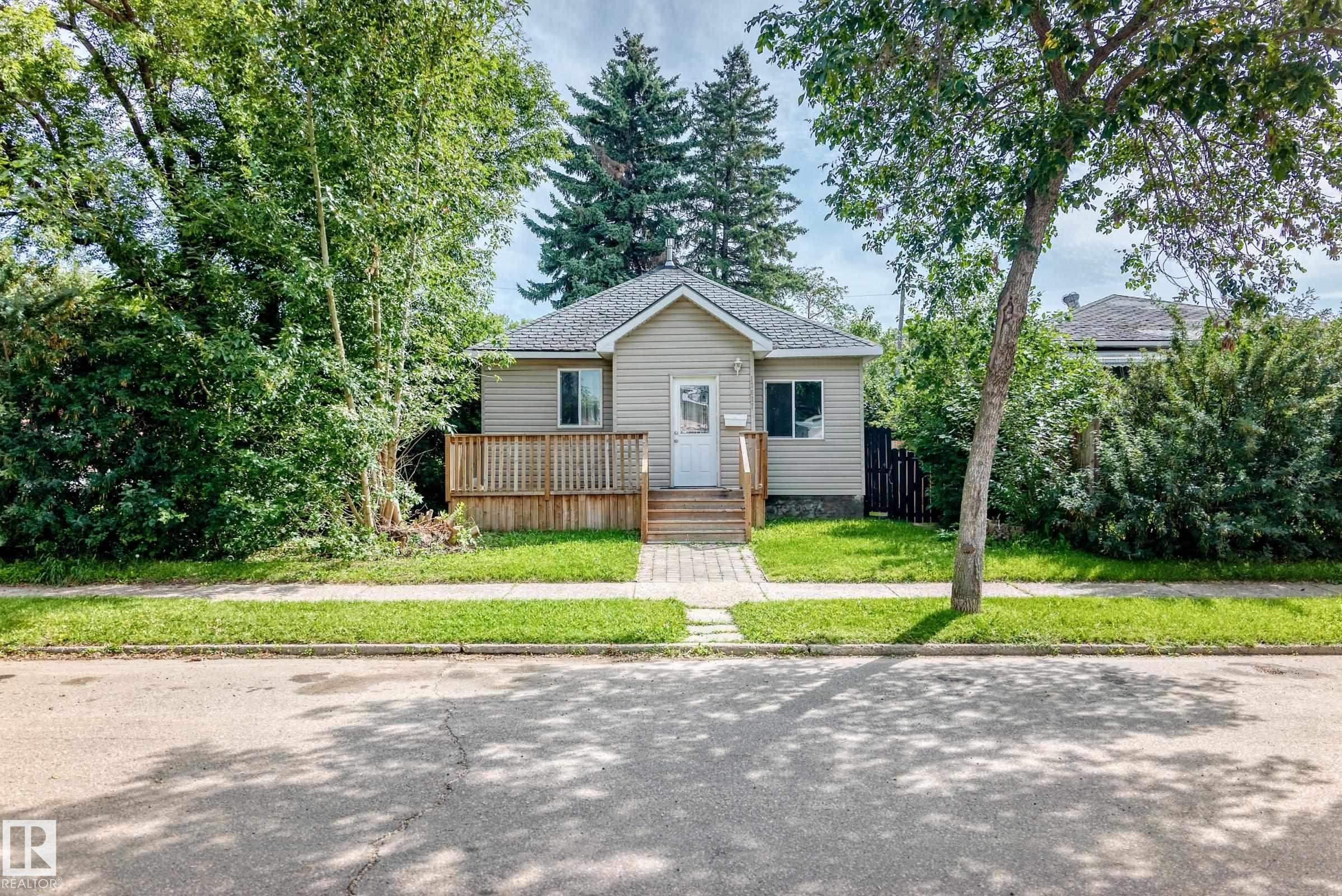 Single-story residence featuring light-colored siding, a dark shingle roof, and a wood-finish deck - 12627 71 Street Nw, Edmonton, AB