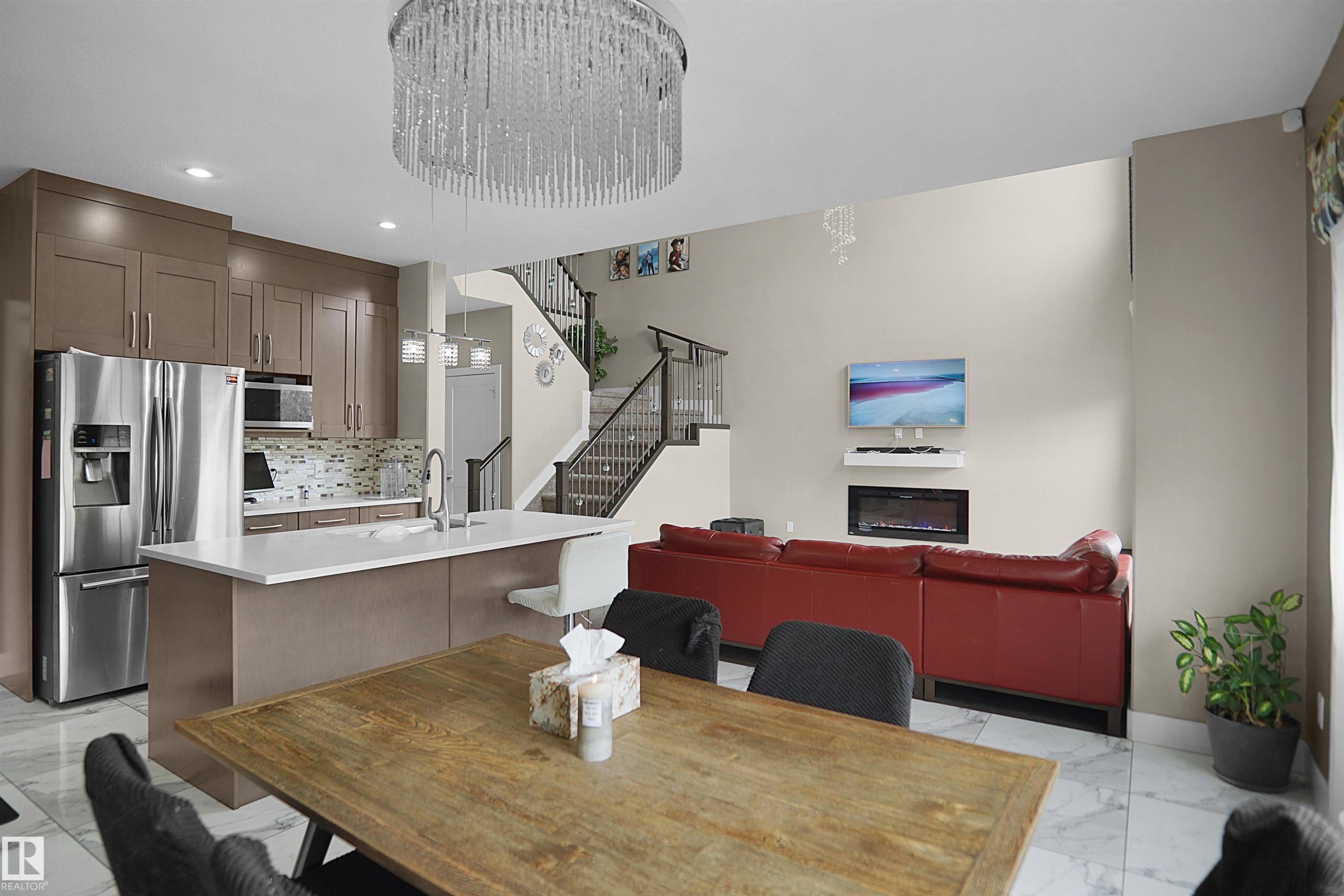 Open-concept living space featuring a modern kitchen with stainless steel appliances, a center island with seating, and a mosaic tile backsplash - 6108 173 Ave, Edmonton, AB - Indoor