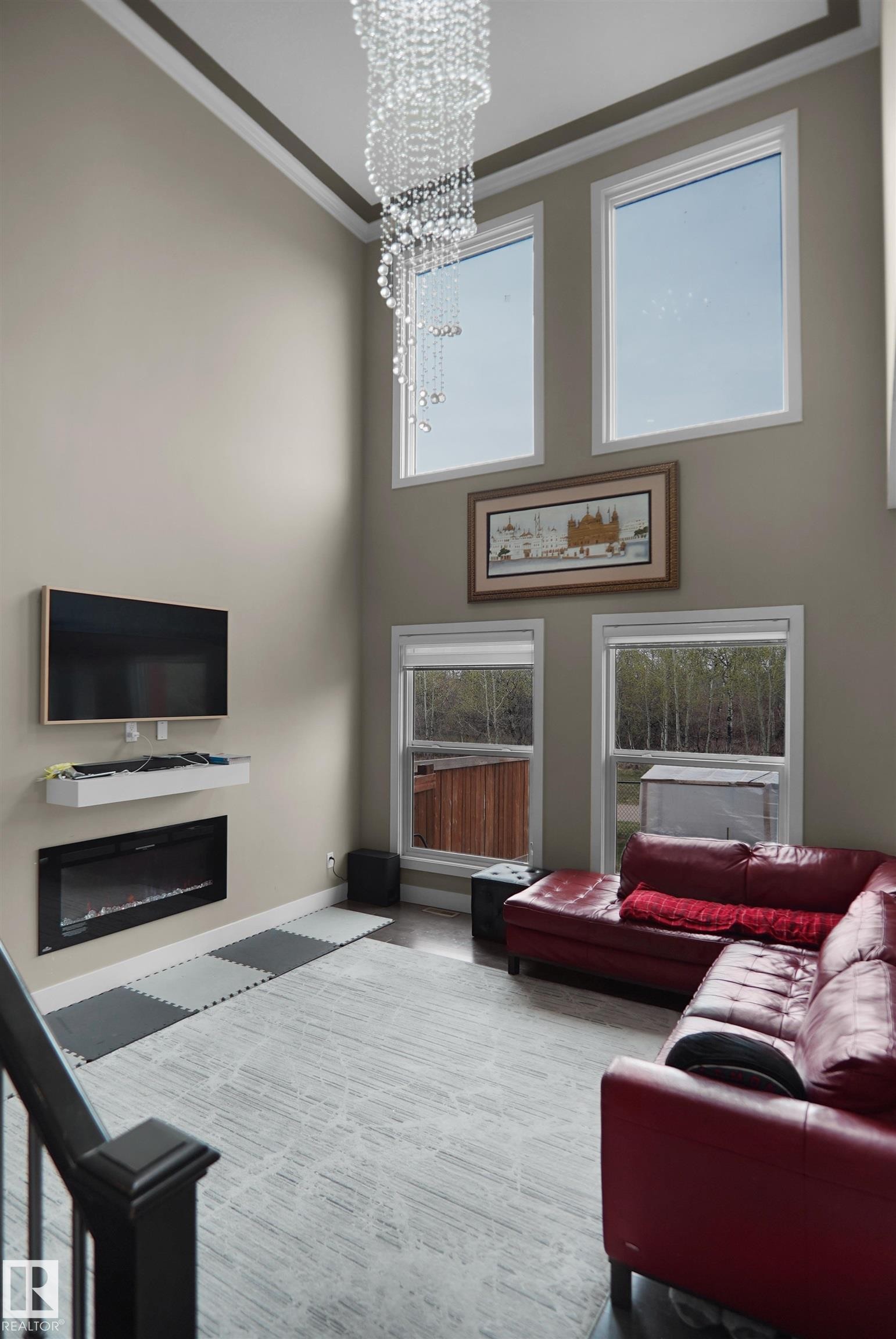 Double-height living space featuring a cascading chandelier, multiple large windows, an integrated electric fireplace, and a wall-mounted media console - 6108 173 Ave, Edmonton, AB - Indoor Photo Showing Living Room With Fireplace