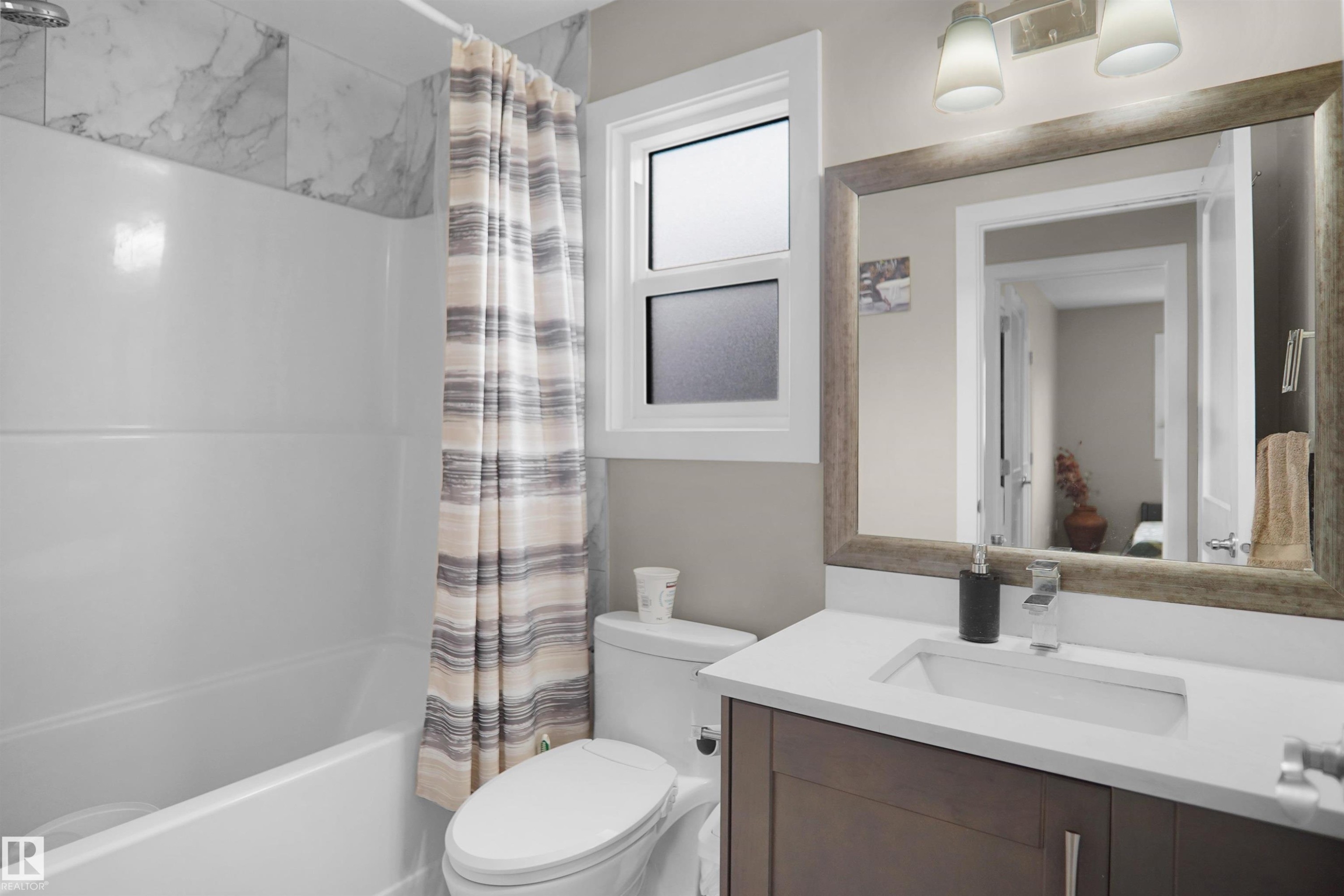 Bathroom featuring a white bathtub, marble-finish wall tiling, a vanity with a white countertop, a rectangular undermount sink, and an overhead vanity light fixture - 6108 173 Ave, Edmonton, AB - Indoor Photo Showing Bathroom