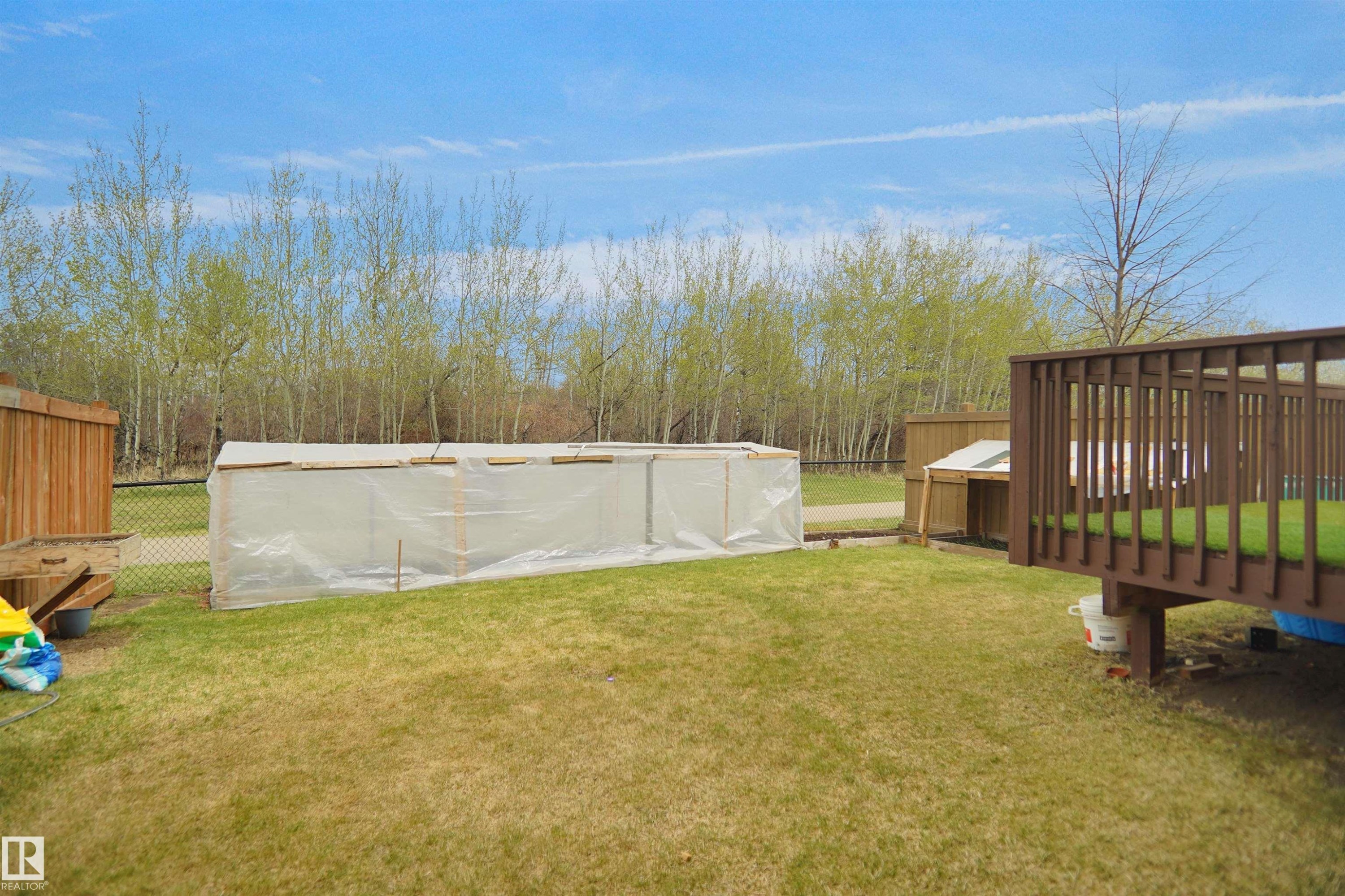 Expansive backyard featuring a fenced perimeter, a raised wooden deck with railings, and a greenhouse structure - 6108 173 Ave, Edmonton, AB - Outdoor With Above Ground Pool With Backyard