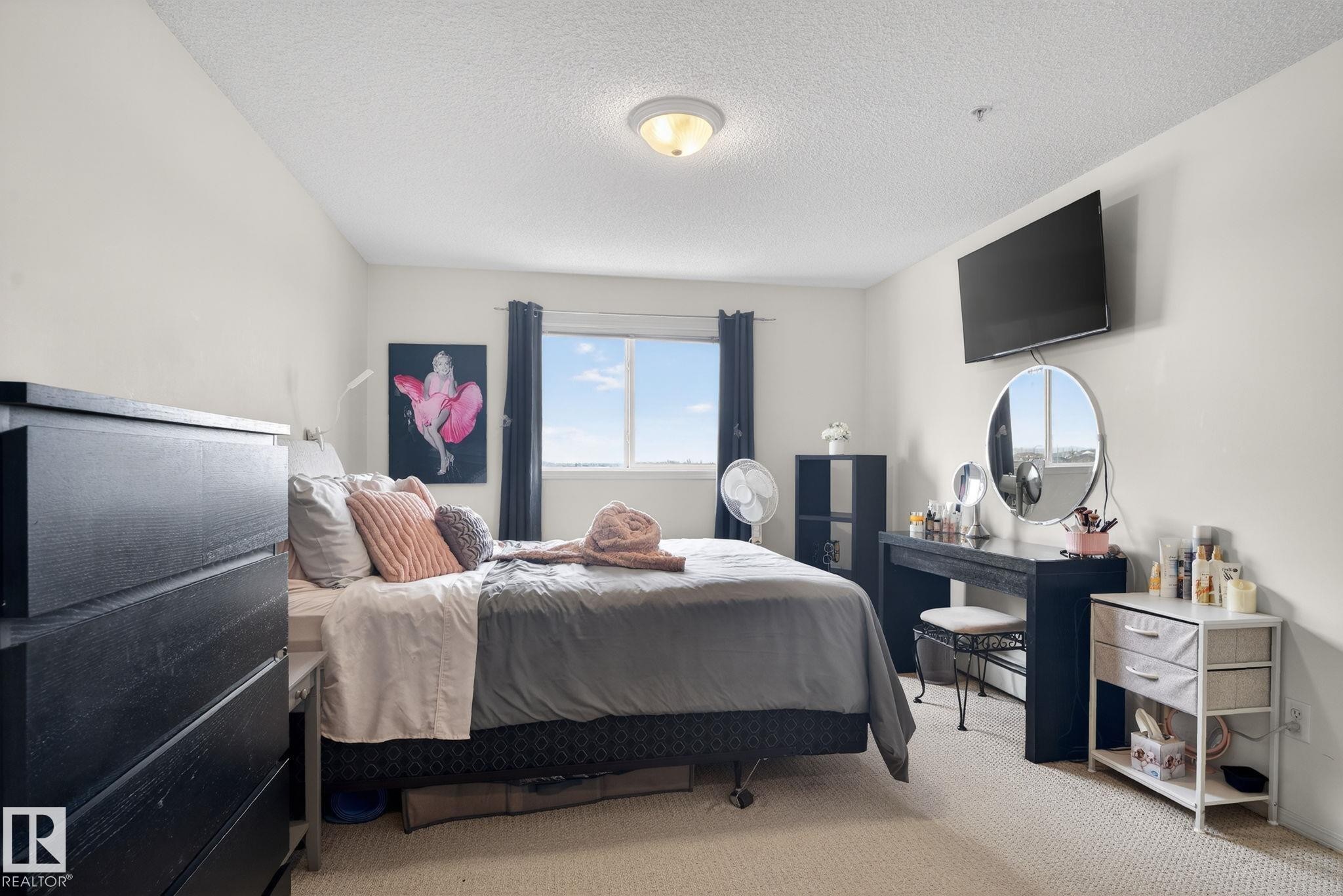 This room features neutral-toned carpeting, a window with dark curtains, and a ceiling light fixture - 423 2430 Guardian Road, Edmonton, AB - Indoor Photo Showing Bedroom