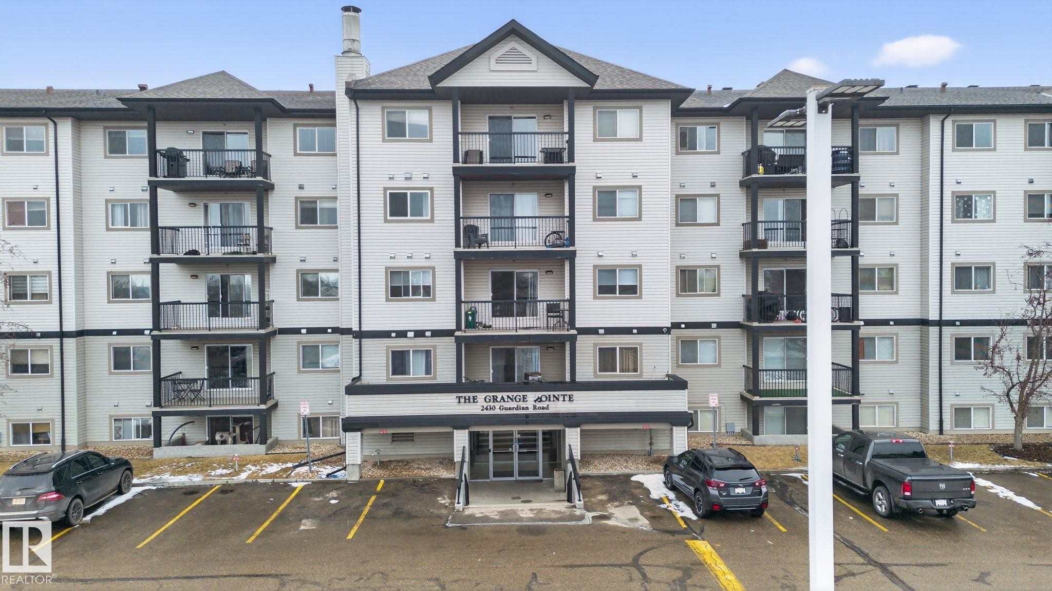 The property features a multi-story building with a light-colored facade, dark-framed windows, and balconies on each level - 423 2430 Guardian Road, Edmonton, AB - Outdoor With Balcony With Facade