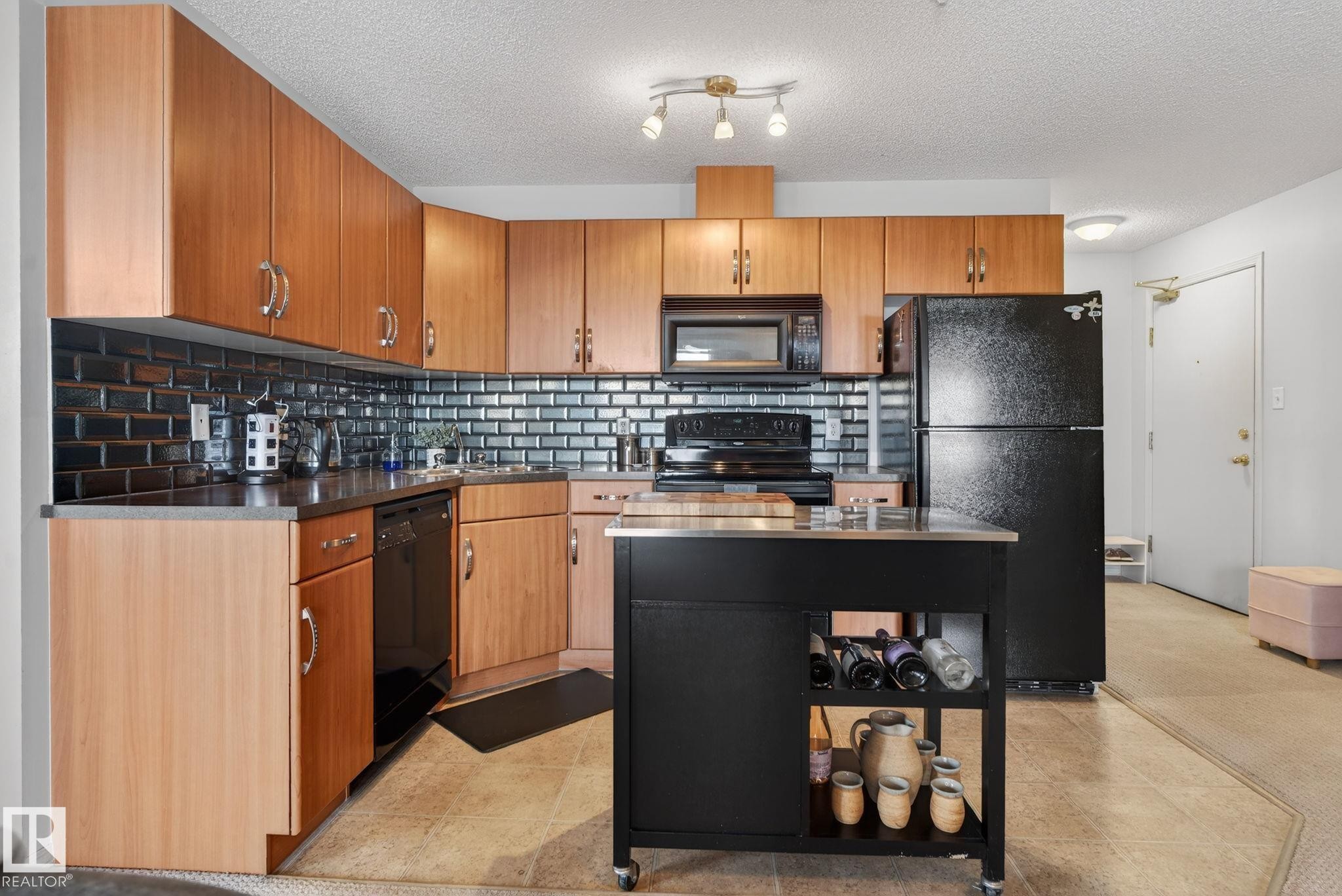 The kitchen features wood cabinetry, dark subway tile backsplash, and a central island with storage - 423 2430 Guardian Road, Edmonton, AB - Indoor Photo Showing Kitchen