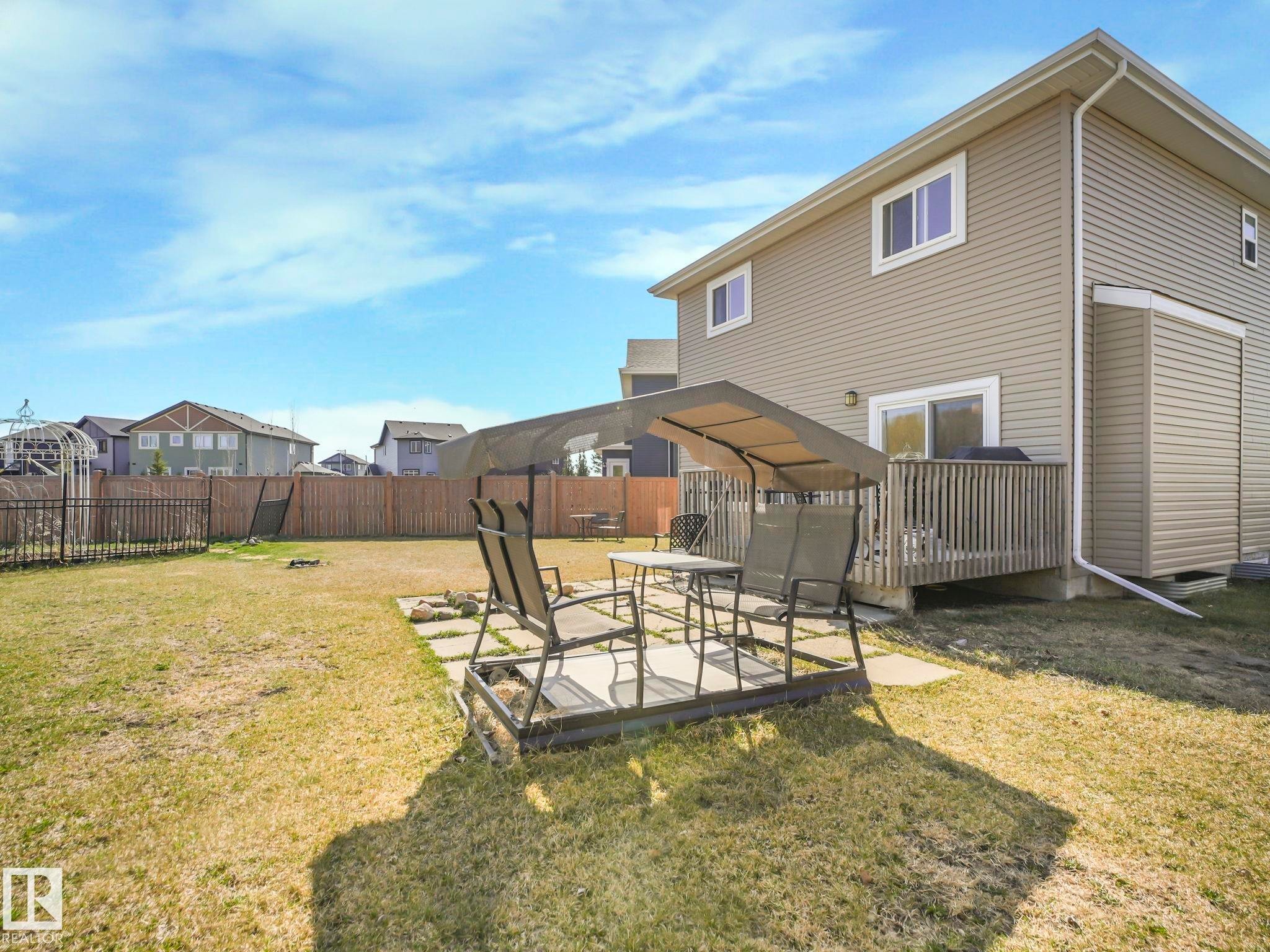 Expansive backyard featuring a privacy fence, wood deck, sliding glass door access, and a paved patio area - 3910 49 Avenue, Beaumont, AB - Outdoor