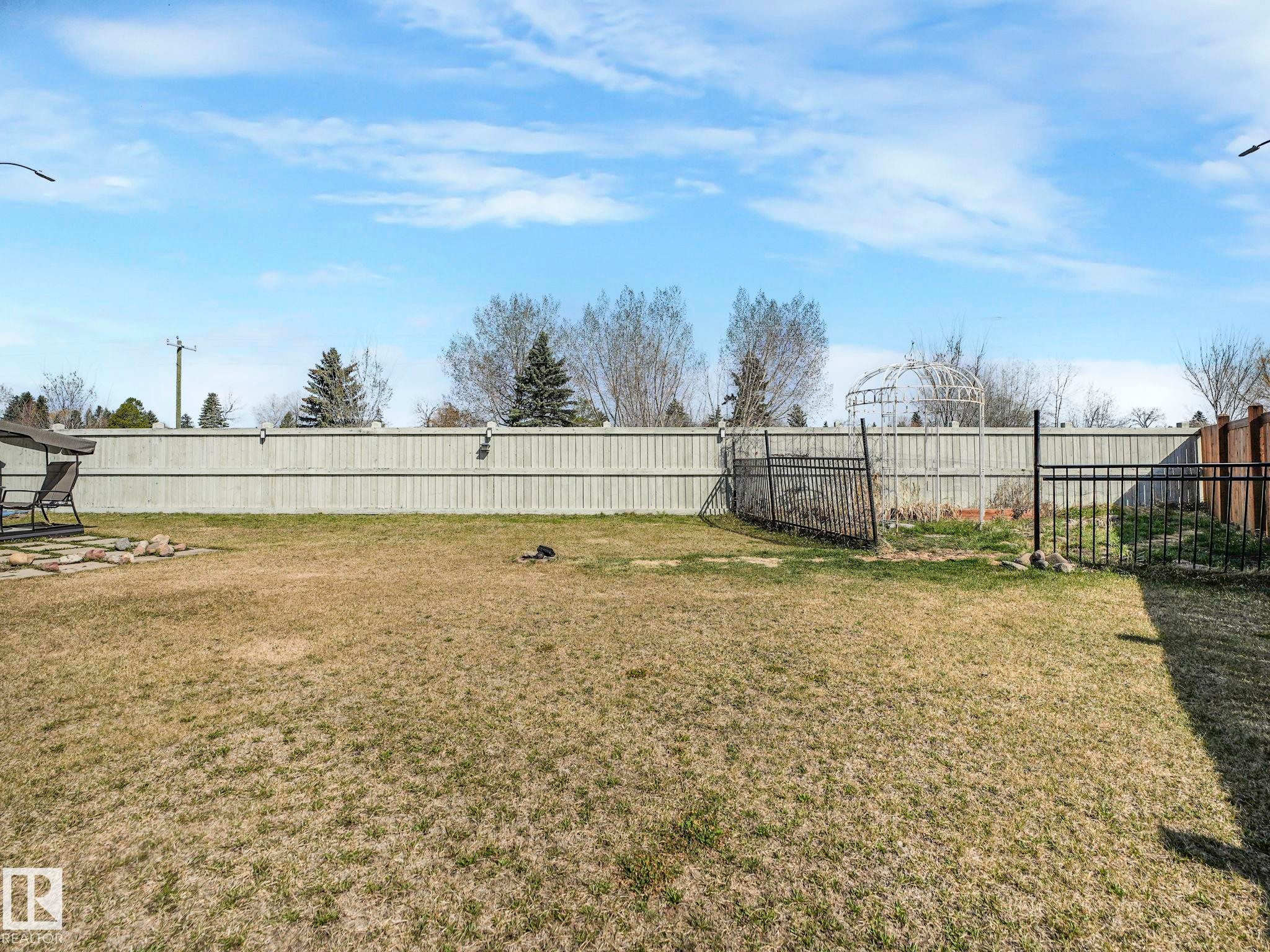 Expansive backyard with a full perimeter fence, featuring a garden area with a decorative archway and a designated fire pit zone - 3910 49 Avenue, Beaumont, AB - Outdoor