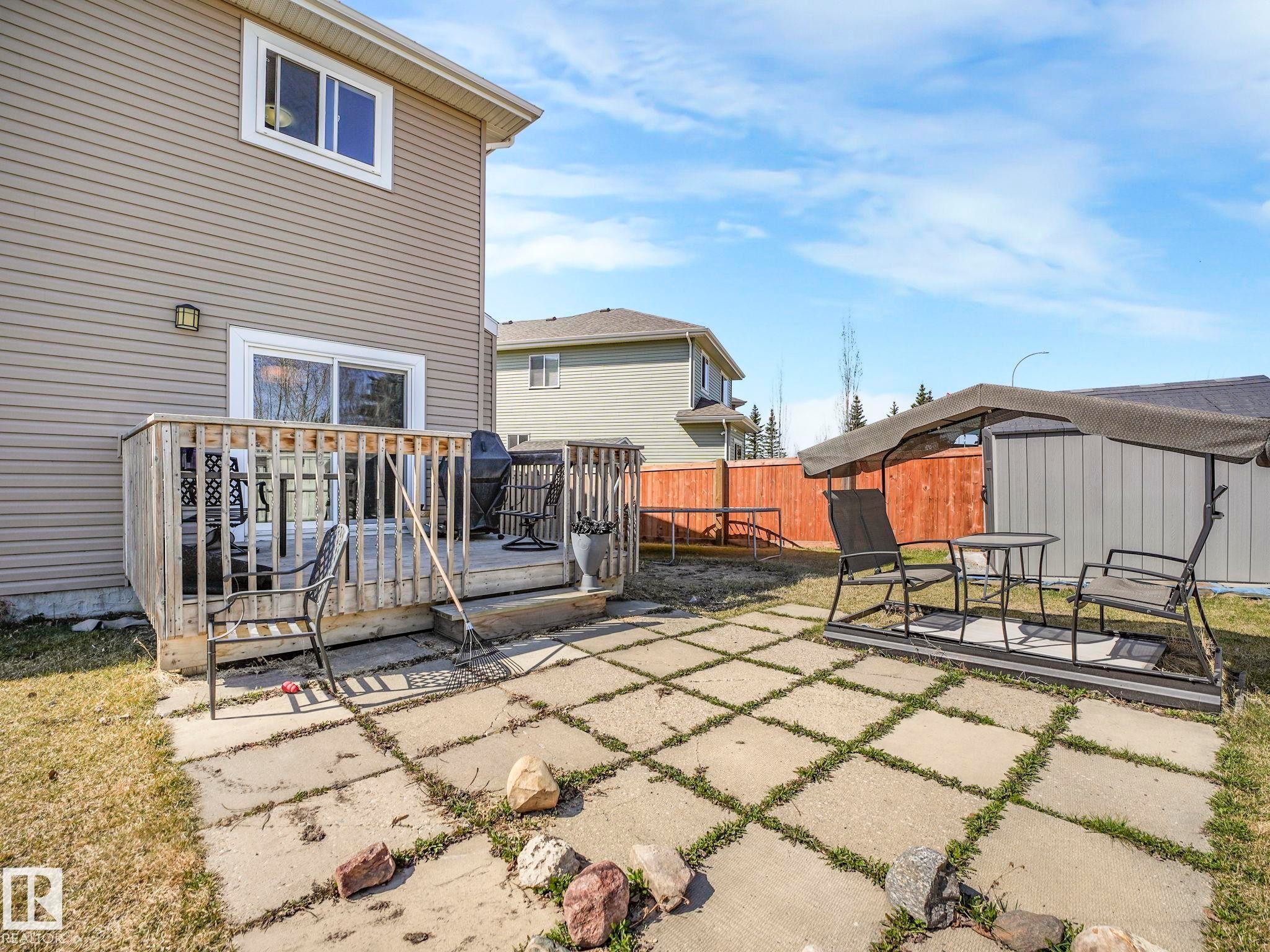 Rear exterior featuring a wooden deck with railing, sliding glass door access, and an adjacent patio with square pavers - 3910 49 Avenue, Beaumont, AB - Outdoor With Deck Patio Veranda