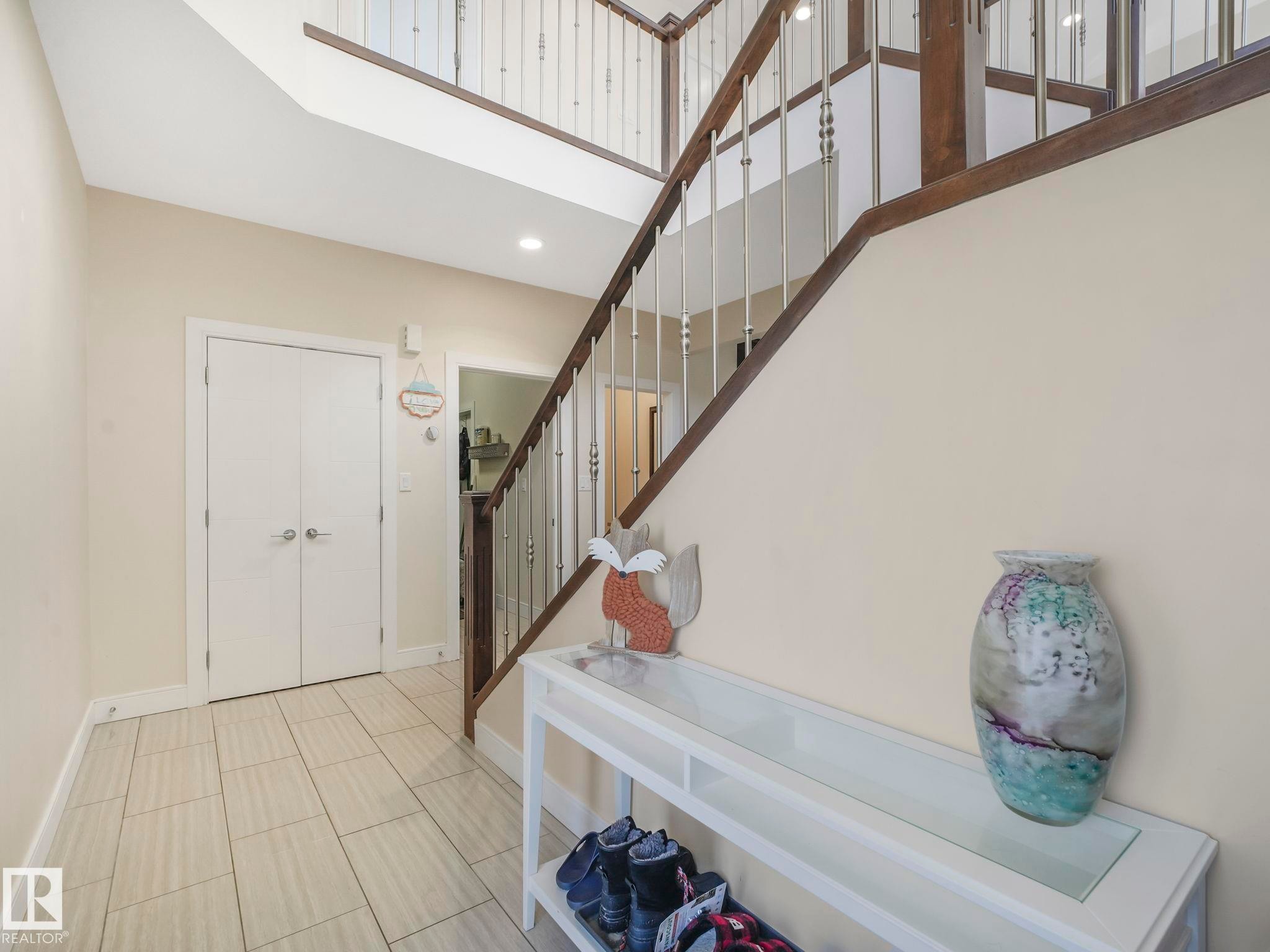 Foyer featuring large format tile flooring, a two-story entryway, and a staircase with wood-finish handrails and metal balusters - 3910 49 Avenue, Beaumont, AB - Indoor Photo Showing Other Room