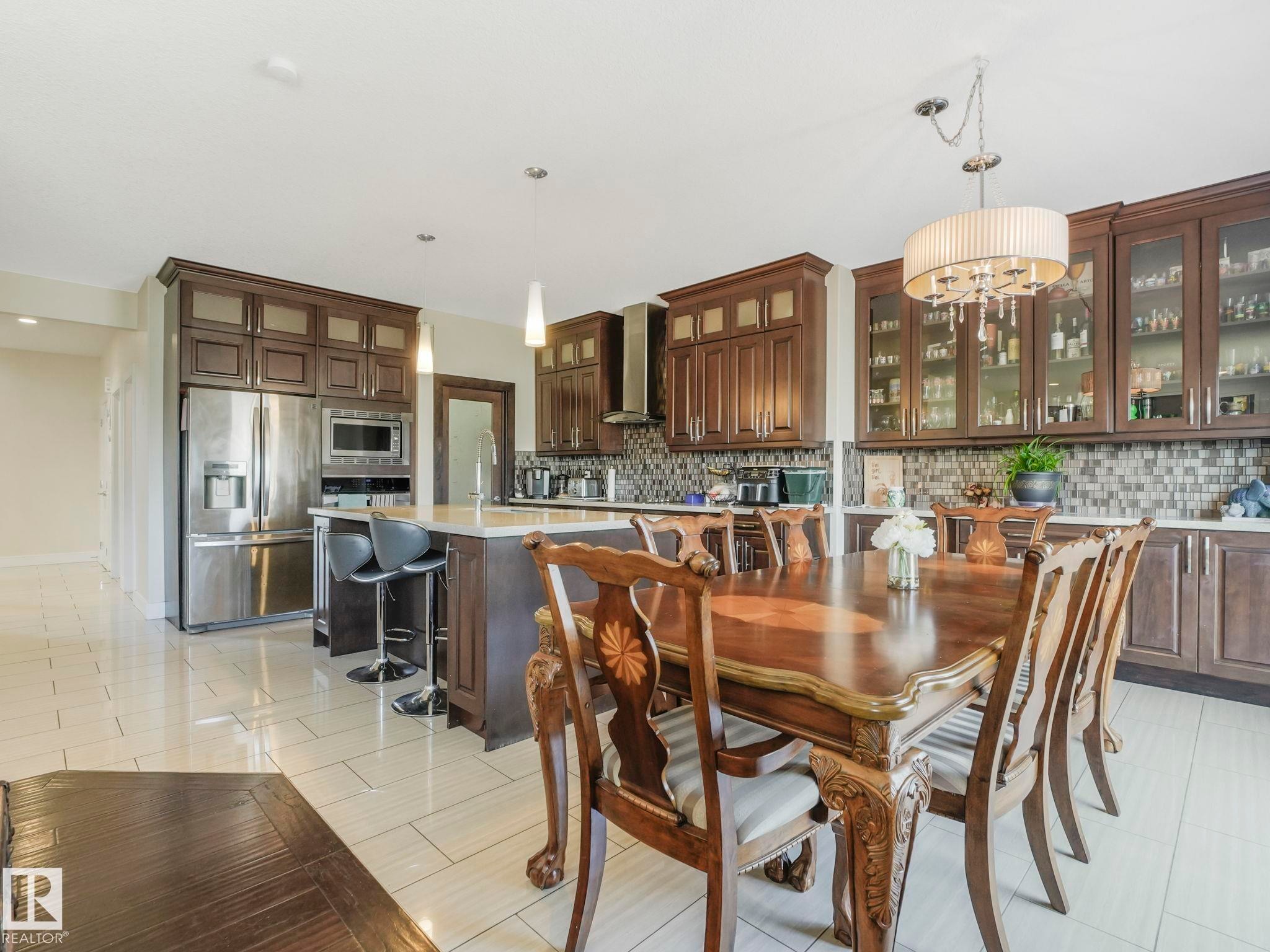 Gourmet kitchen and dining area featuring dark wood cabinetry, stainless steel appliances, a center island with seating, mosaic tile backsplash, and light-toned floor tile - 3910 49 Avenue, Beaumont, AB - Indoor Photo Showing Dining Room