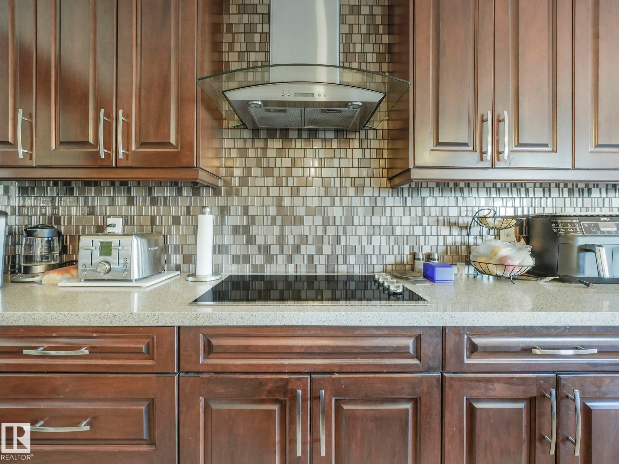 Kitchen featuring rich wood cabinetry, a mosaic tile backsplash, a built-in cooktop, a stainless steel range hood, and light-toned countertops - 3910 49 Avenue, Beaumont, AB - Indoor Photo Showing Kitchen