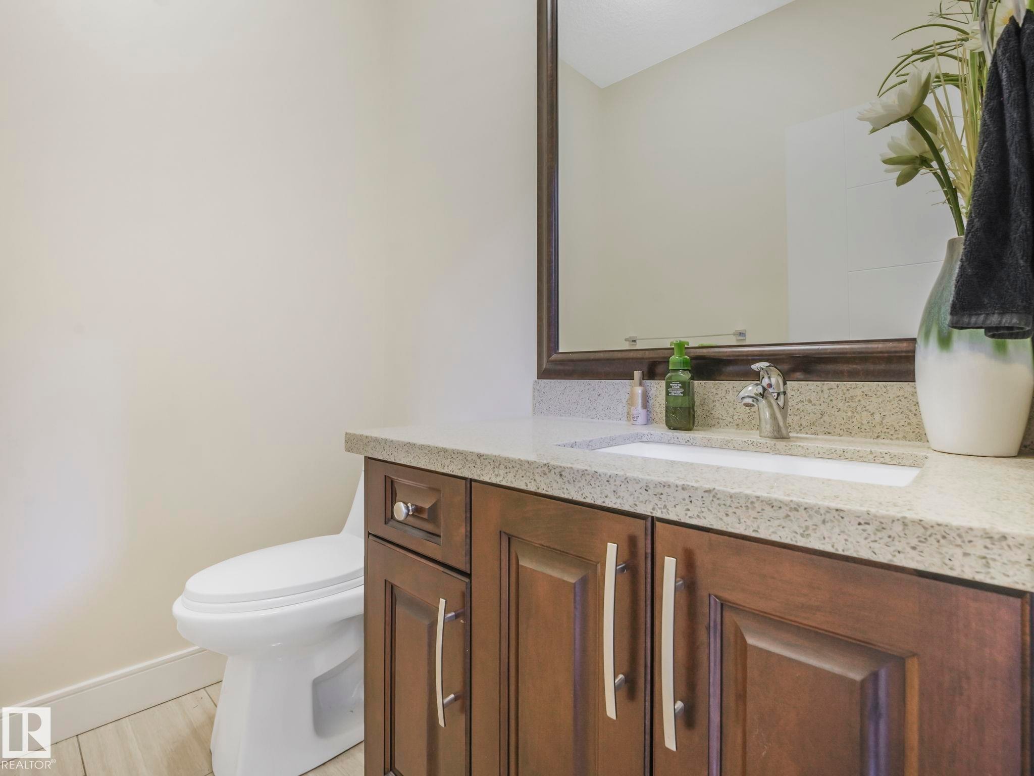 Bathroom vanity featuring a granite-style countertop, undermount sink, and wood-finish cabinetry with brushed nickel hardware - 3910 49 Avenue, Beaumont, AB - Indoor Photo Showing Bathroom