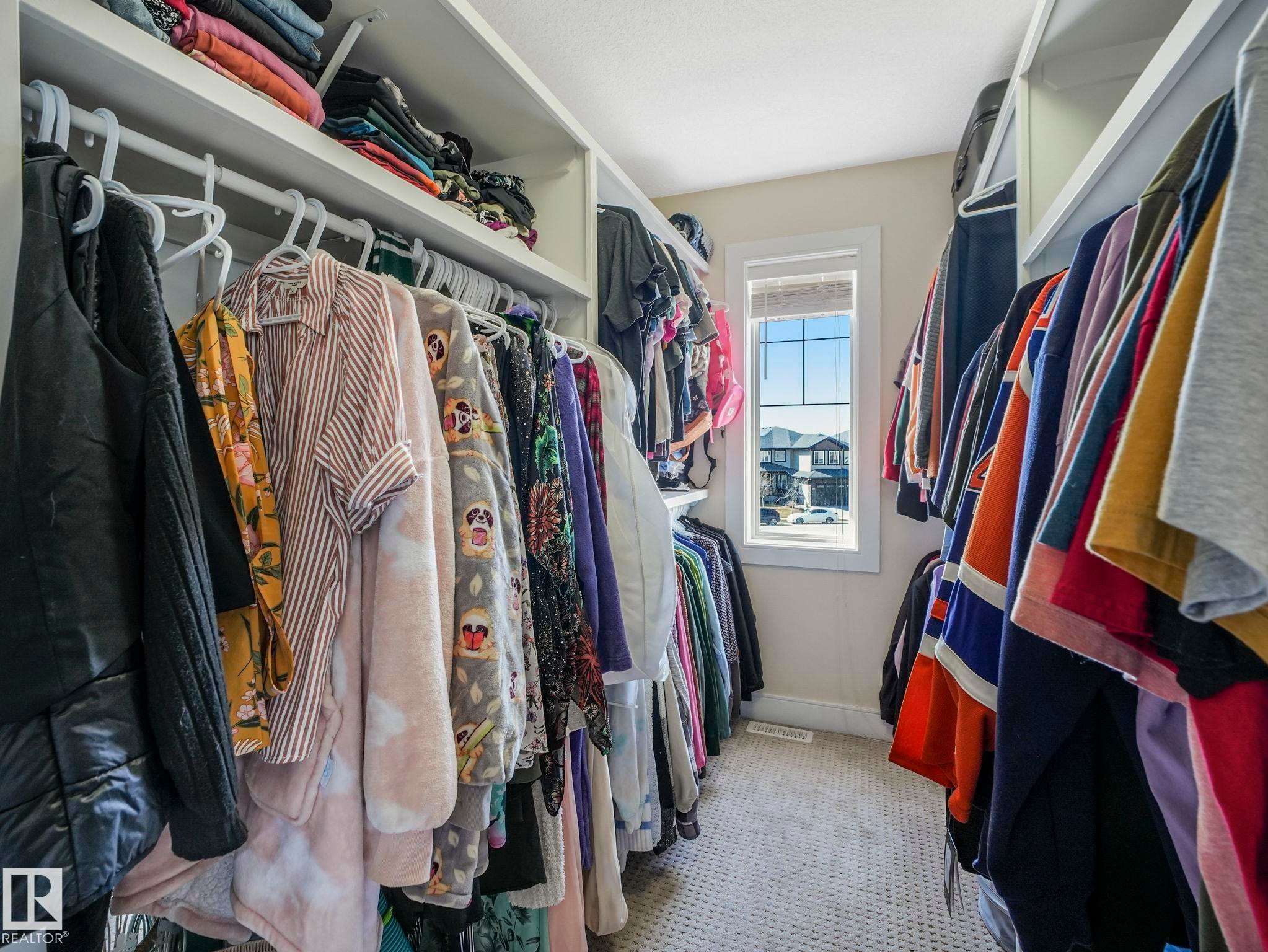 Walk-in closet featuring built-in shelving, hanging rods, light-colored walls, patterned carpeting, and a window with blinds - 3910 49 Avenue, Beaumont, AB - Indoor With Storage