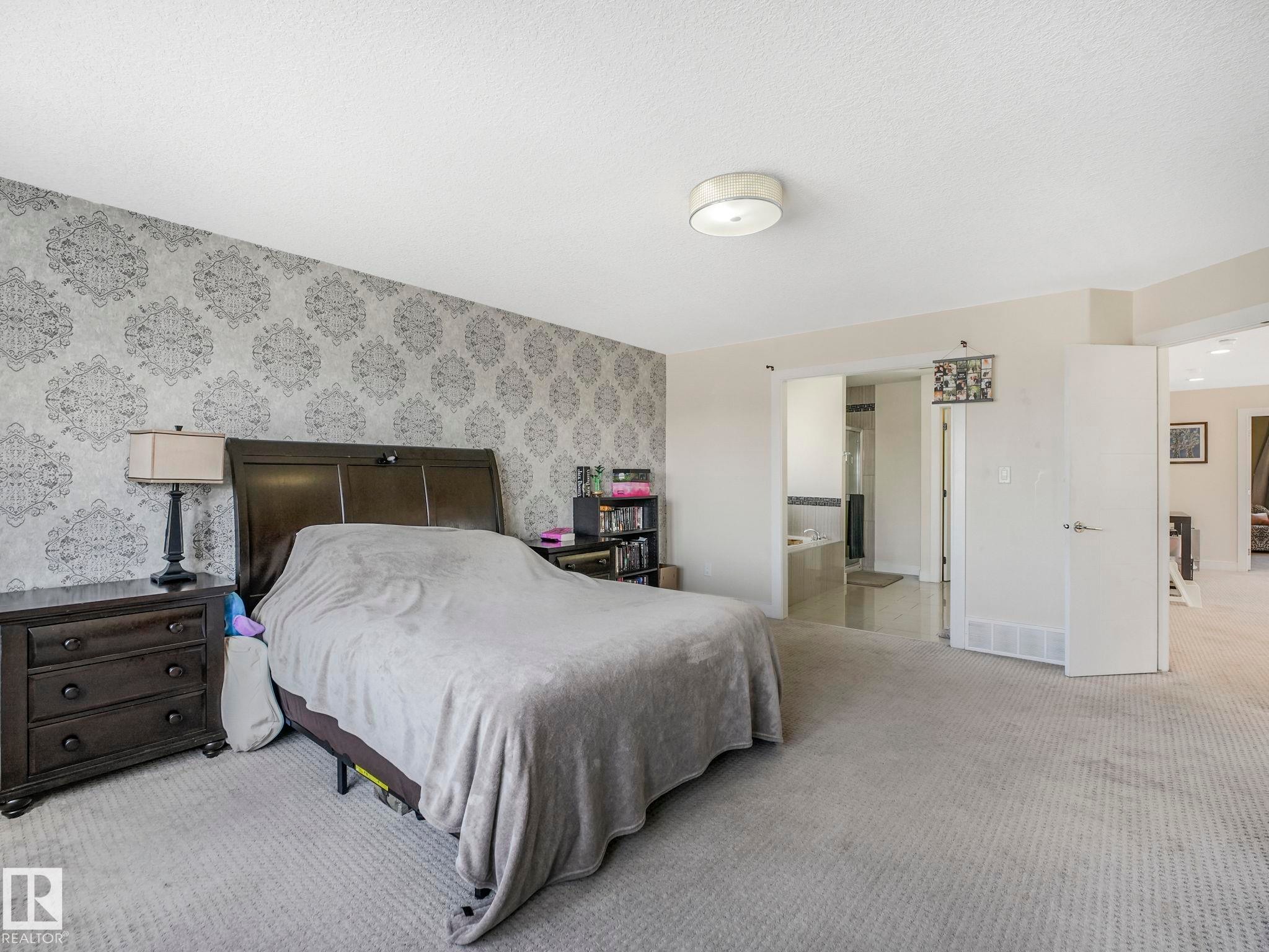 Bedroom featuring patterned accent wall, light-toned carpeting, and a flush-mount ceiling light - 3910 49 Avenue, Beaumont, AB - Indoor Photo Showing Bedroom