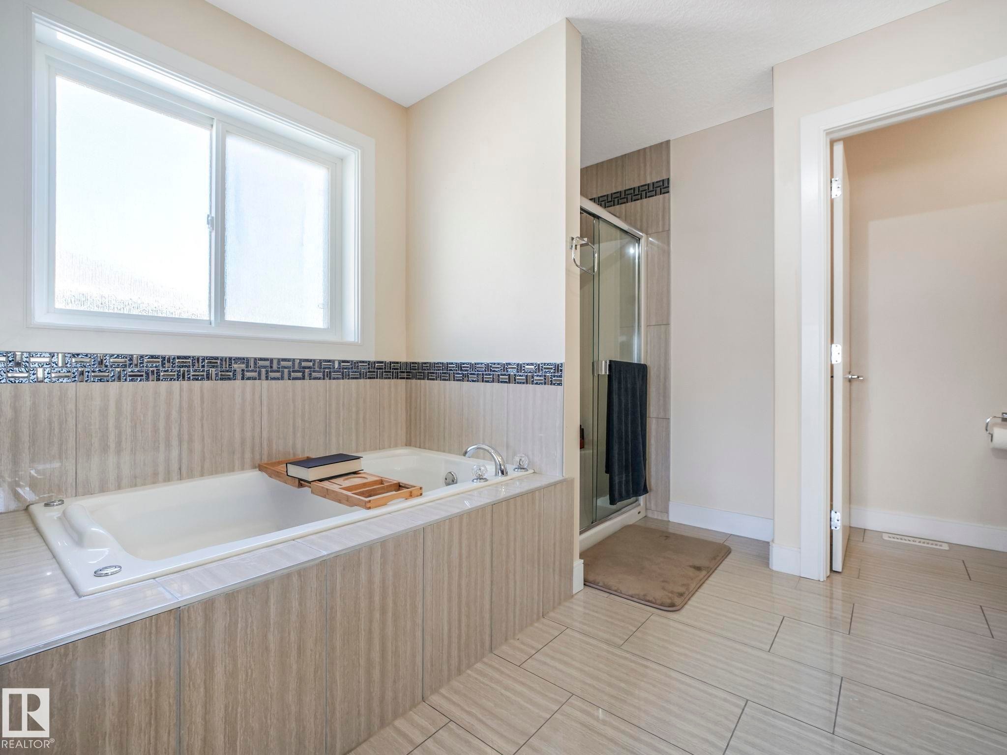 Soaking tub with a tiled surround featuring a decorative mosaic accent - 3910 49 Avenue, Beaumont, AB - Indoor Photo Showing Bathroom